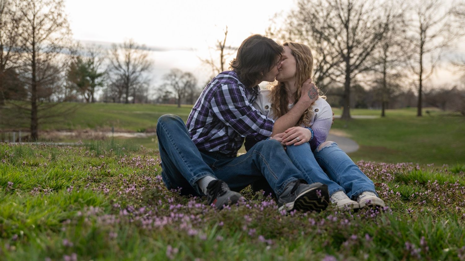 A couple sharing an intimate moment while sitting together on grass during sunset.