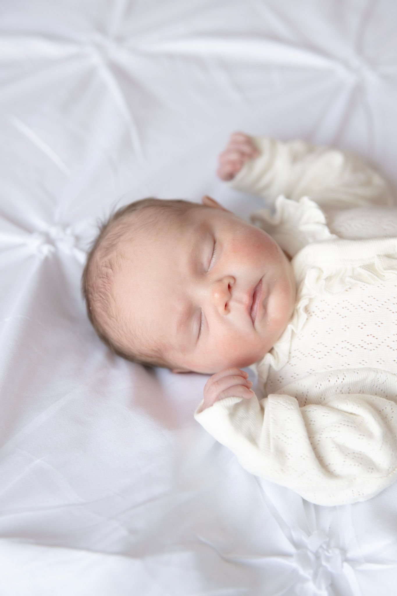 Peaceful newborn sleeping in white clothing on soft white bedding.