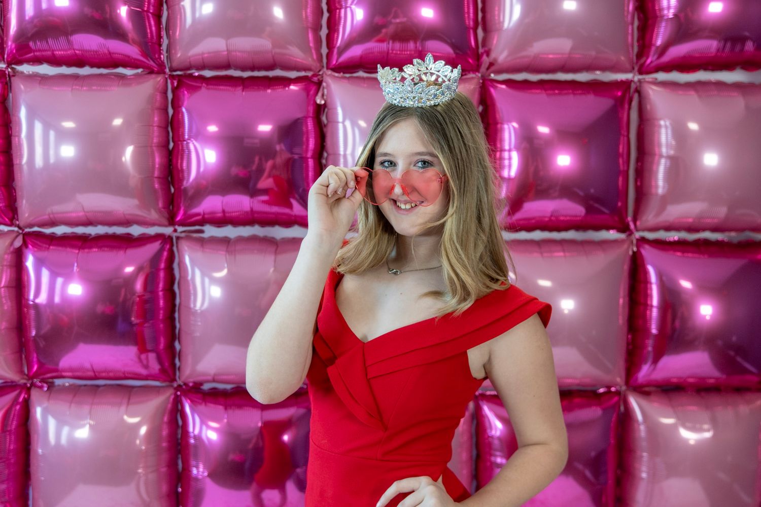 Festive poses in red formal wear against metallic pink balloon wall.