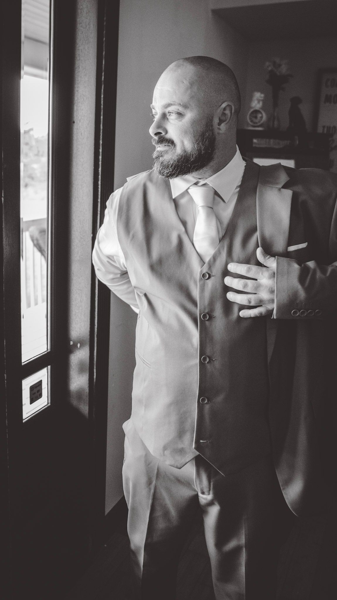 Black and white photo series of a groom in a light colored suit posing by a window.