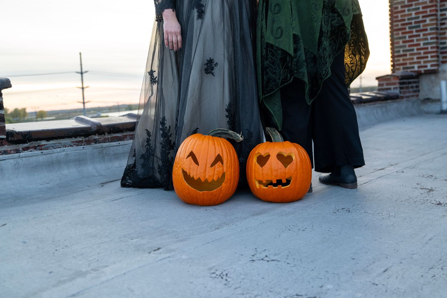 Two carved jack-o'-lanterns sit on ground next to long flowing dresses.