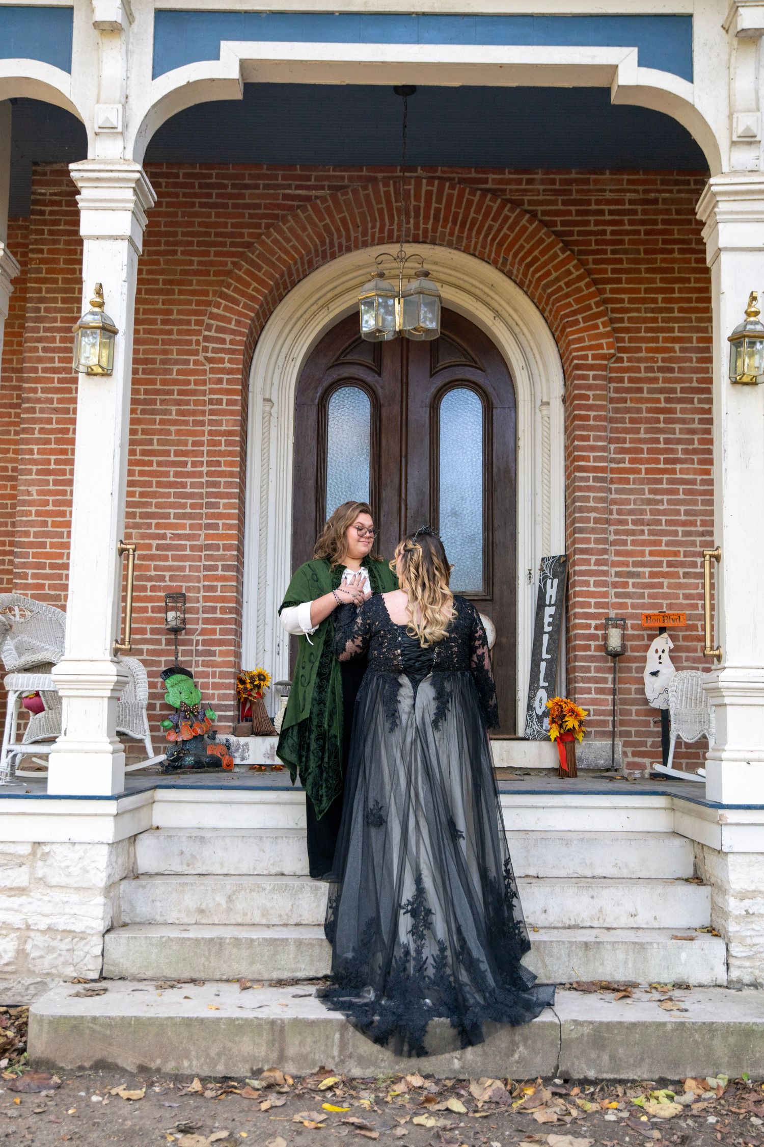 Couple in coordinating outfits poses playfully across stone steps of a vintage brick building.