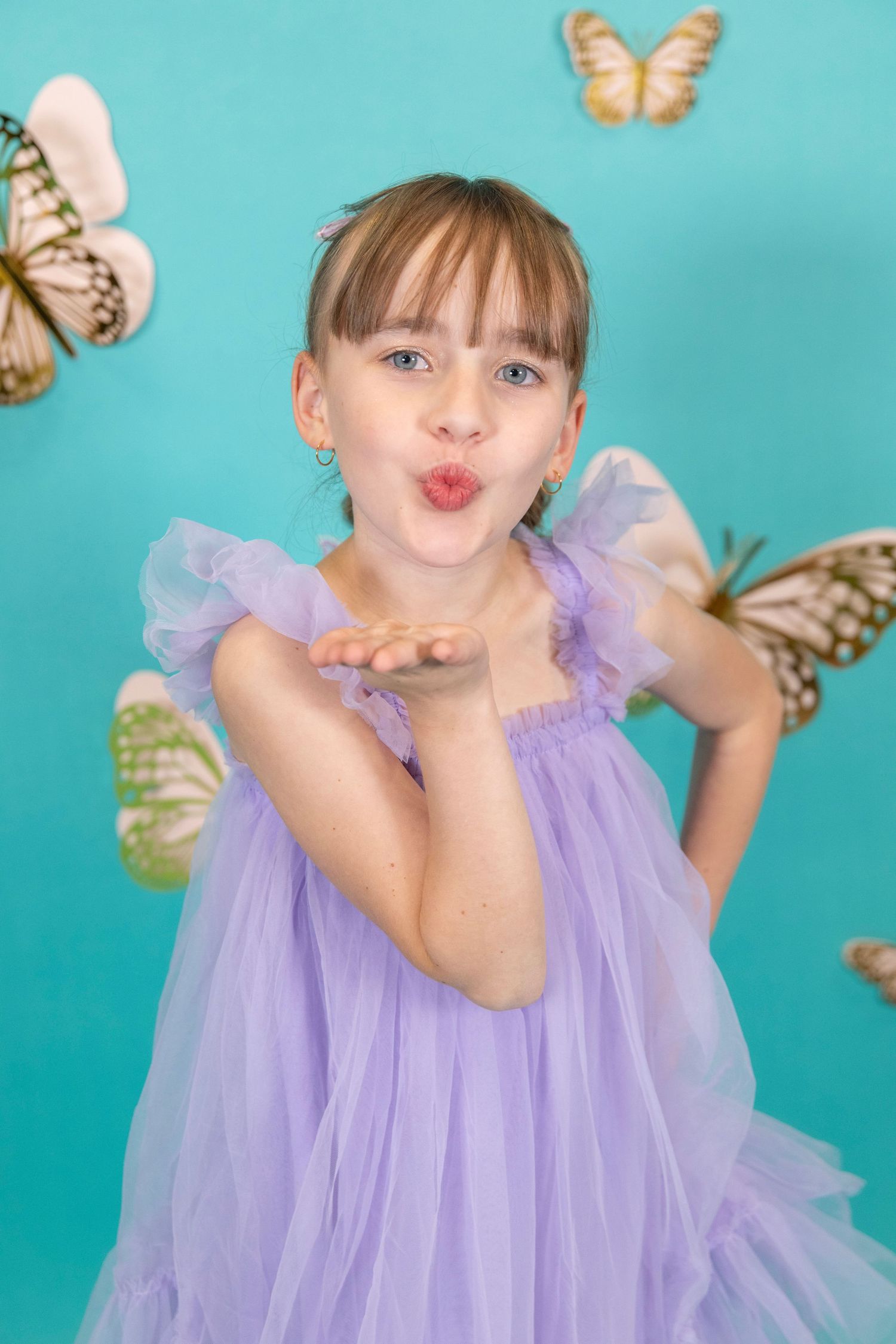 Playful pose in a lilac tulle dress surrounded by golden butterflies on turquoise.