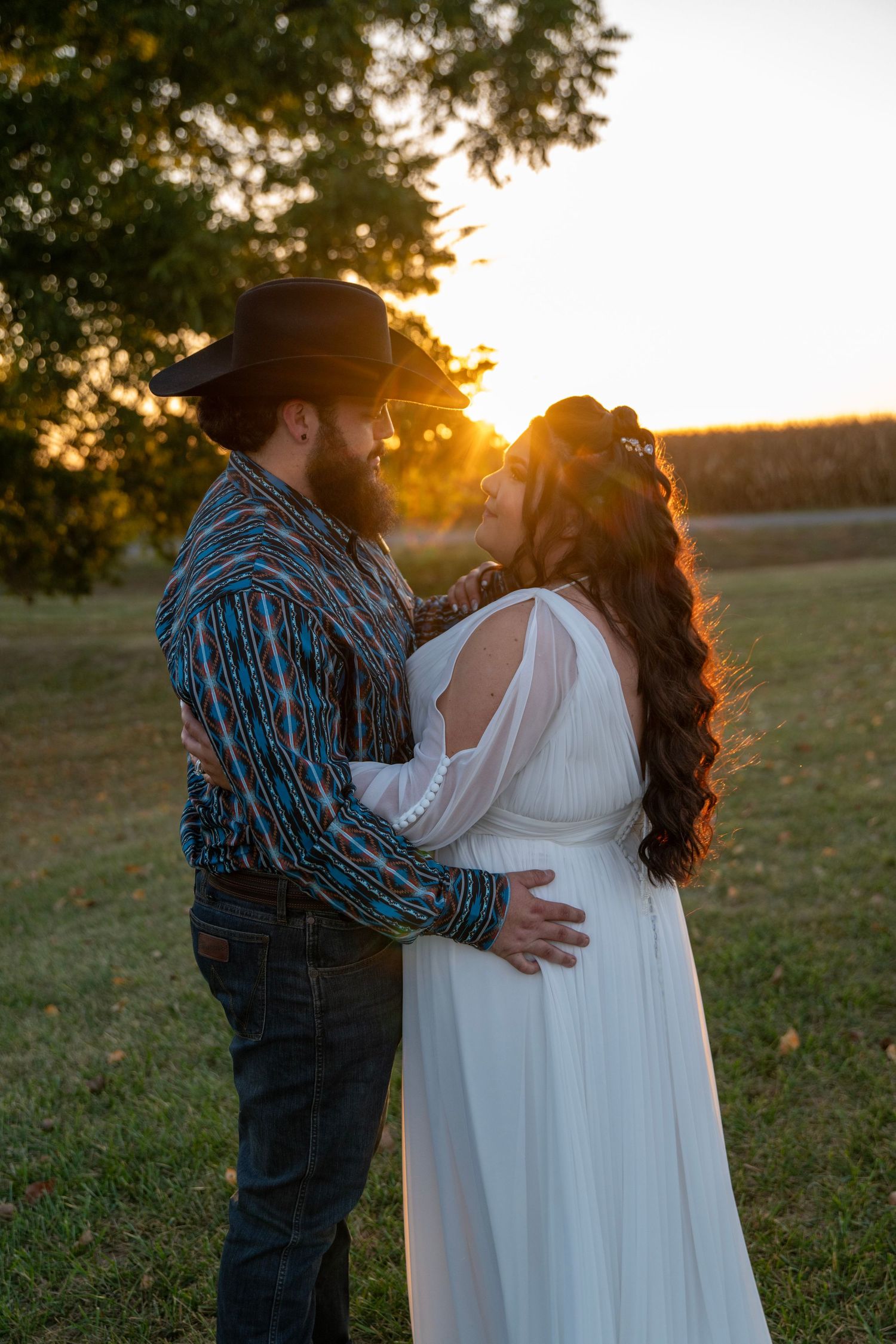 Couple shares intimate moment against sunset backdrop during outdoor autumn wedding.