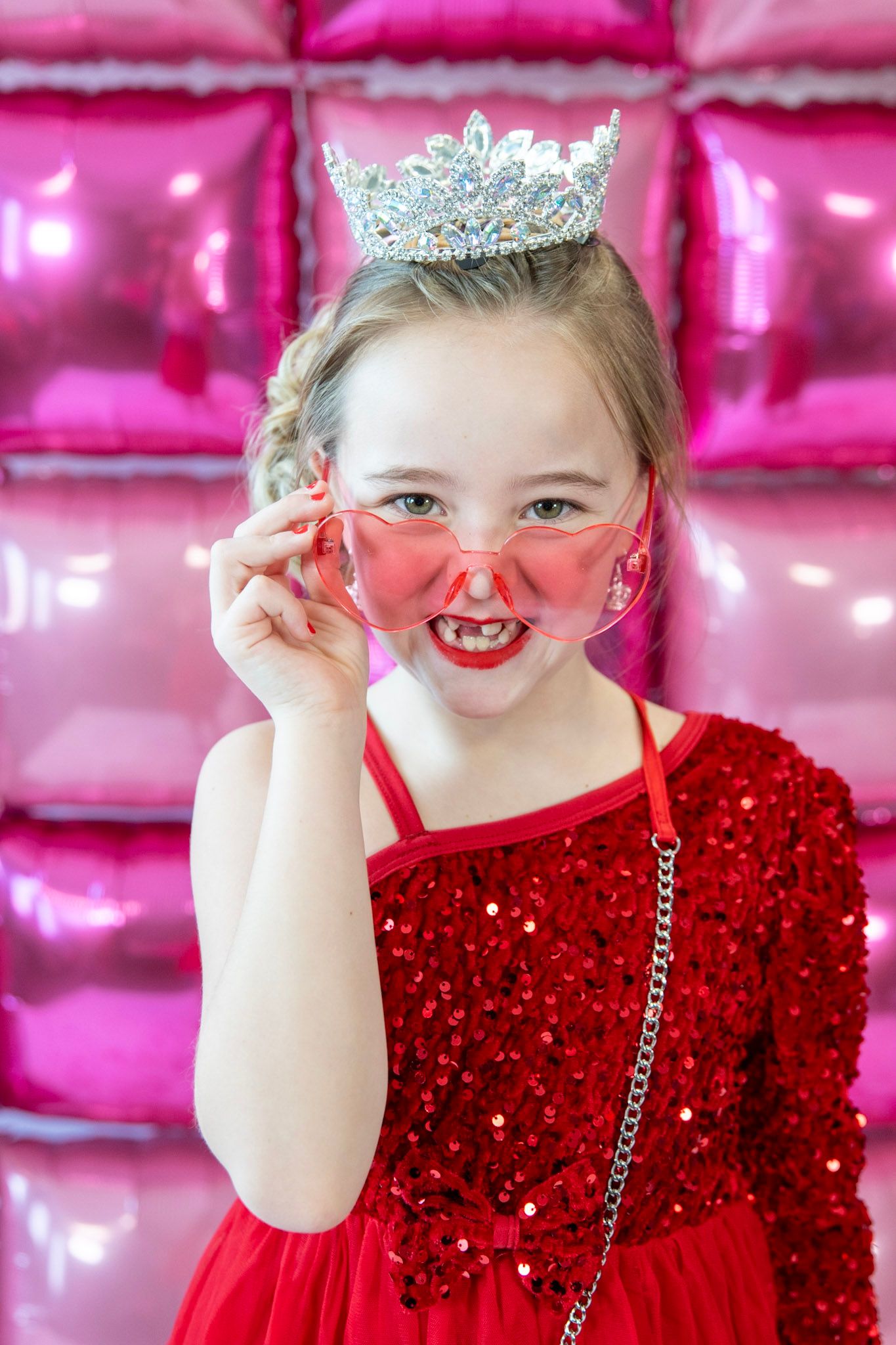 Sparkly red dress and tiara against pink backdrop with playful poses.