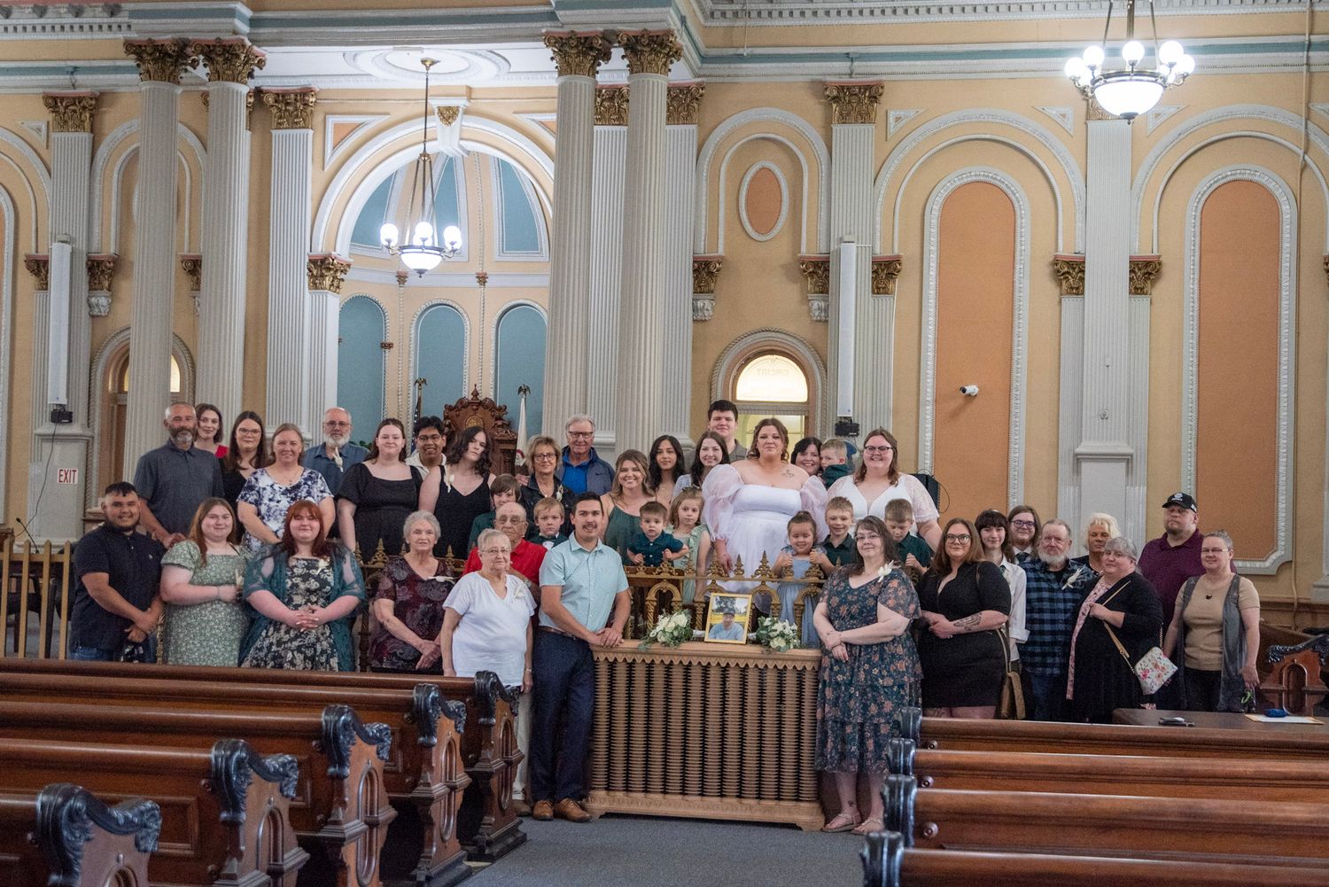 A large group photo of wedding guests gathered in an ornate church with classical architecture and columns.