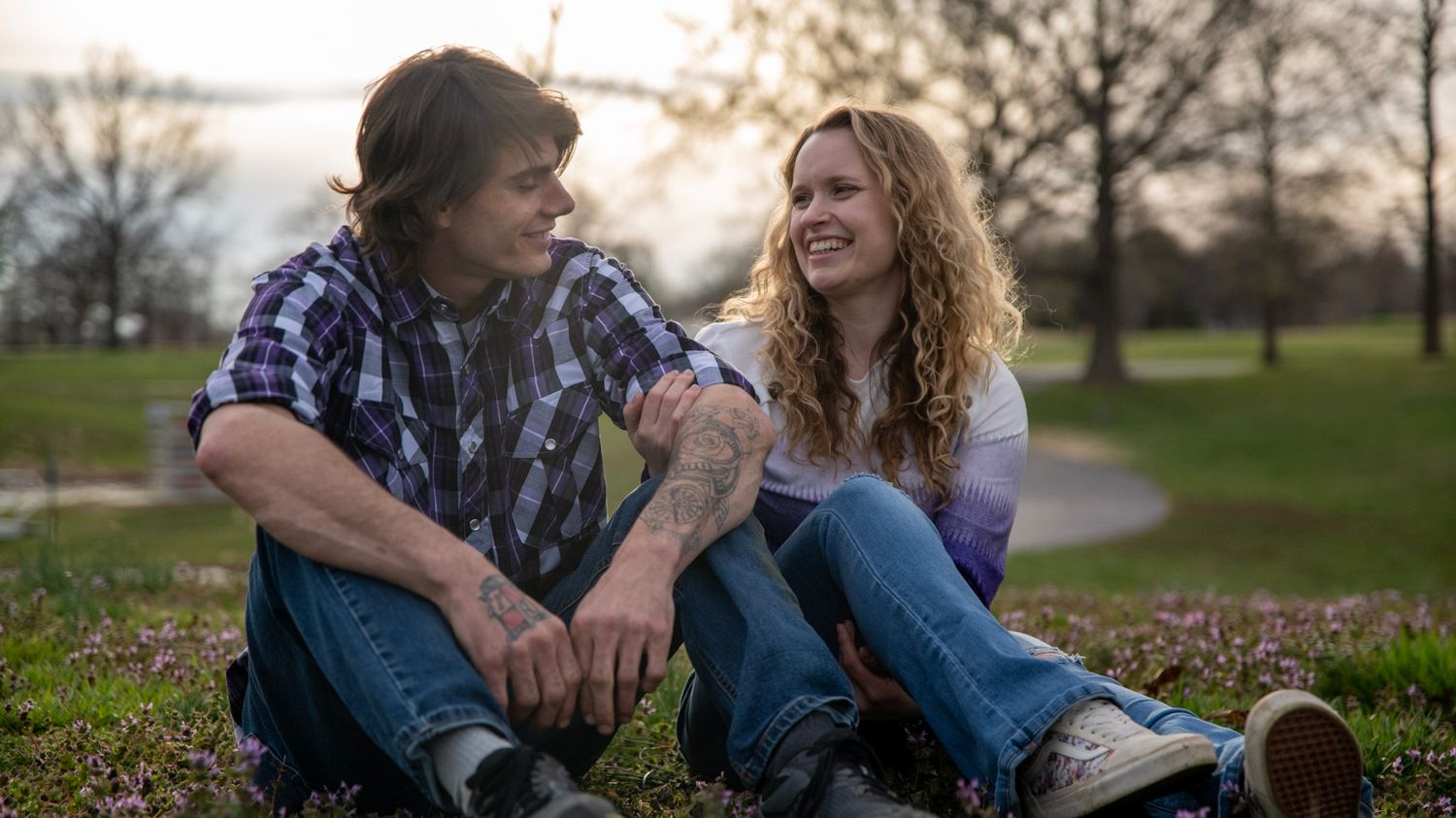 A couple sitting on grass at sunset sharing laughter and conversation in a park.