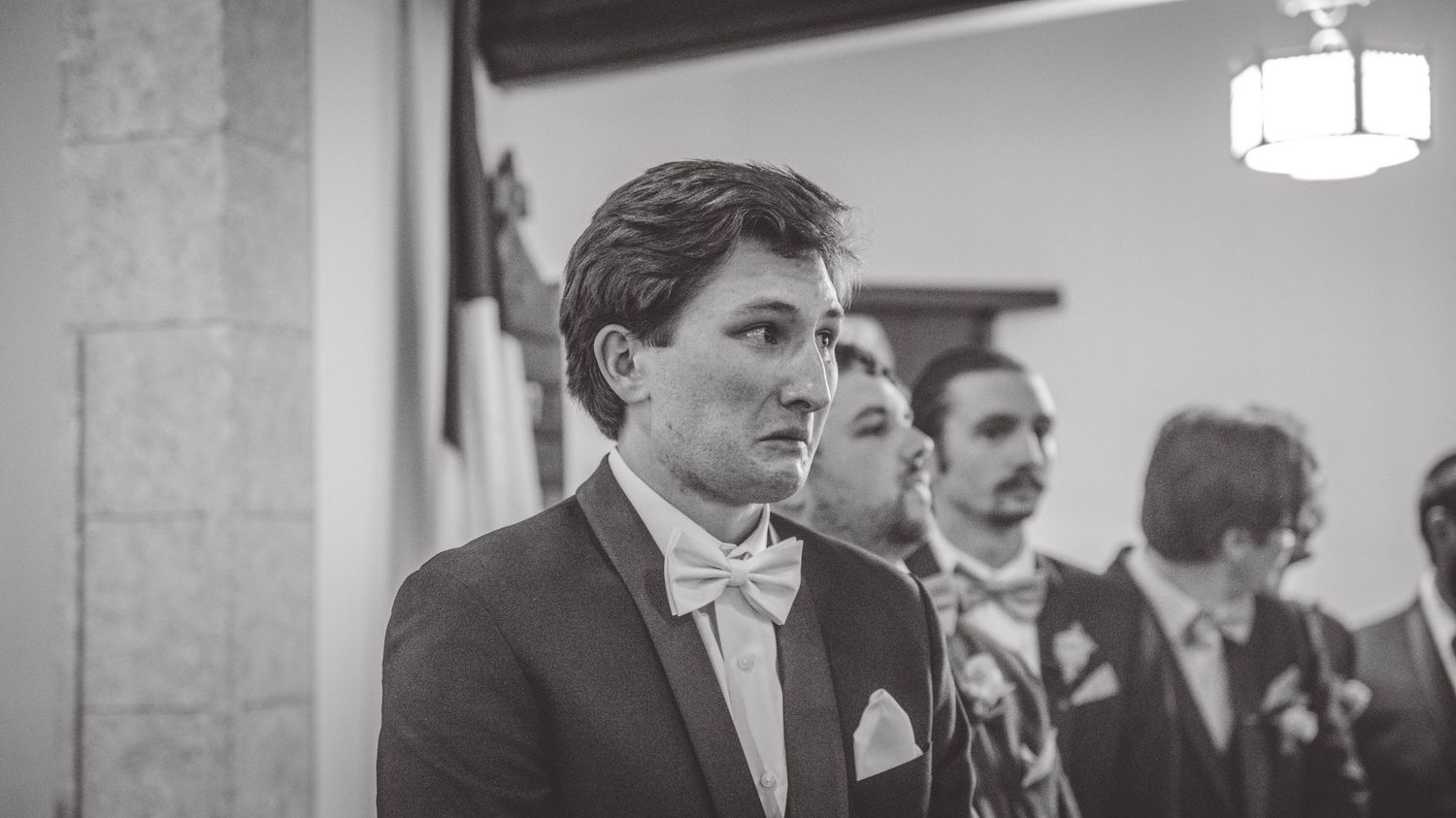 Black and white photo of groomsmen in formal attire at a wedding venue.