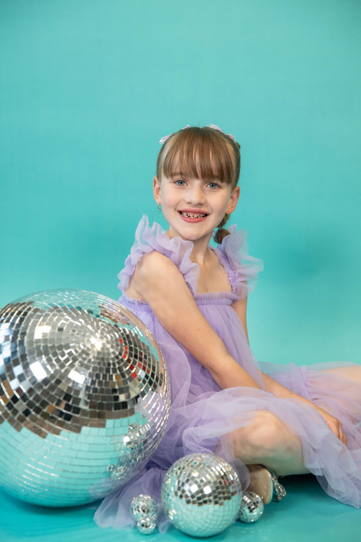 Mirror balls arranged with person in lavender tulle dress against turquoise background.