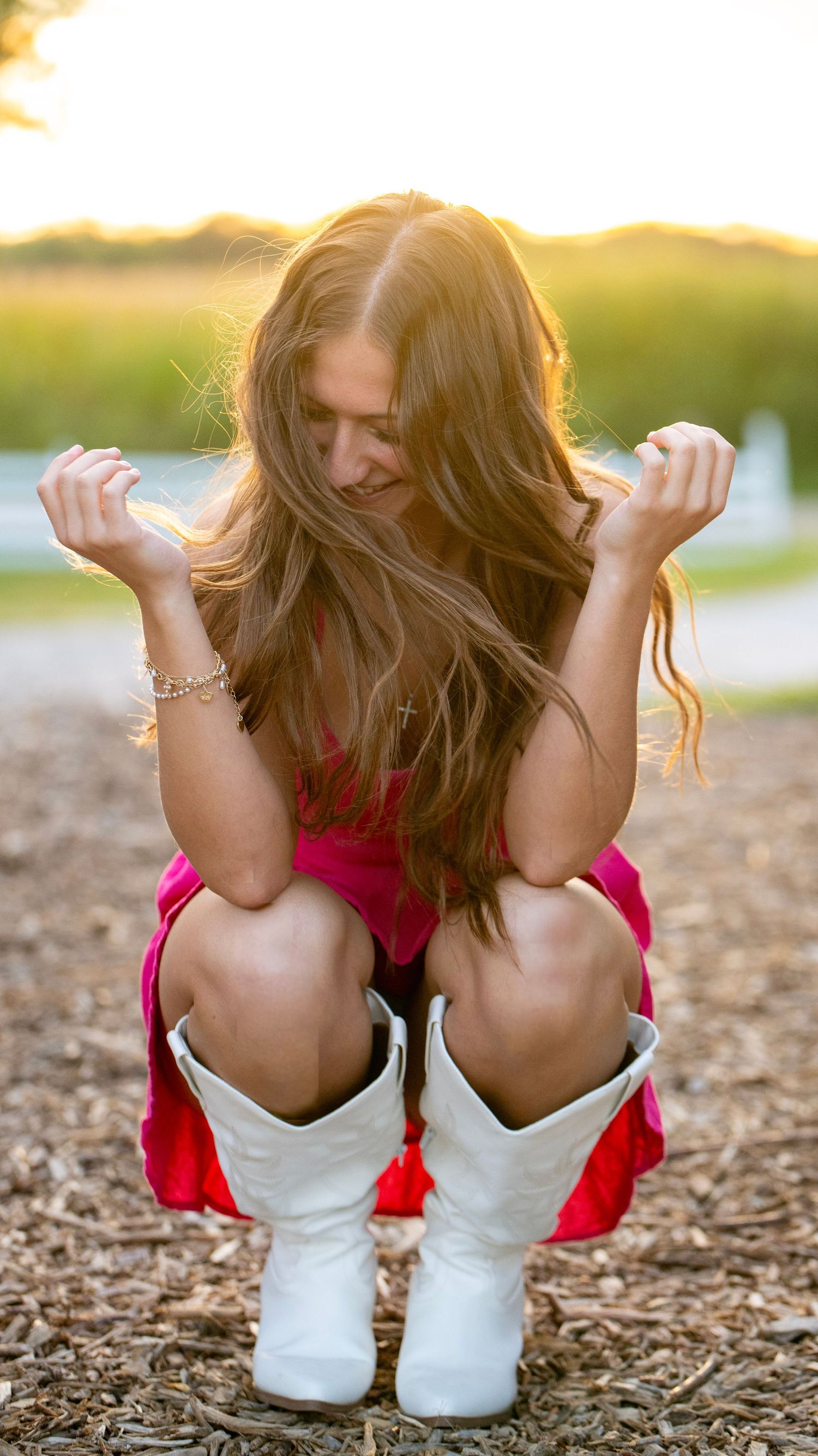 Playful crouching pose in white boots and pink dress at golden hour.
