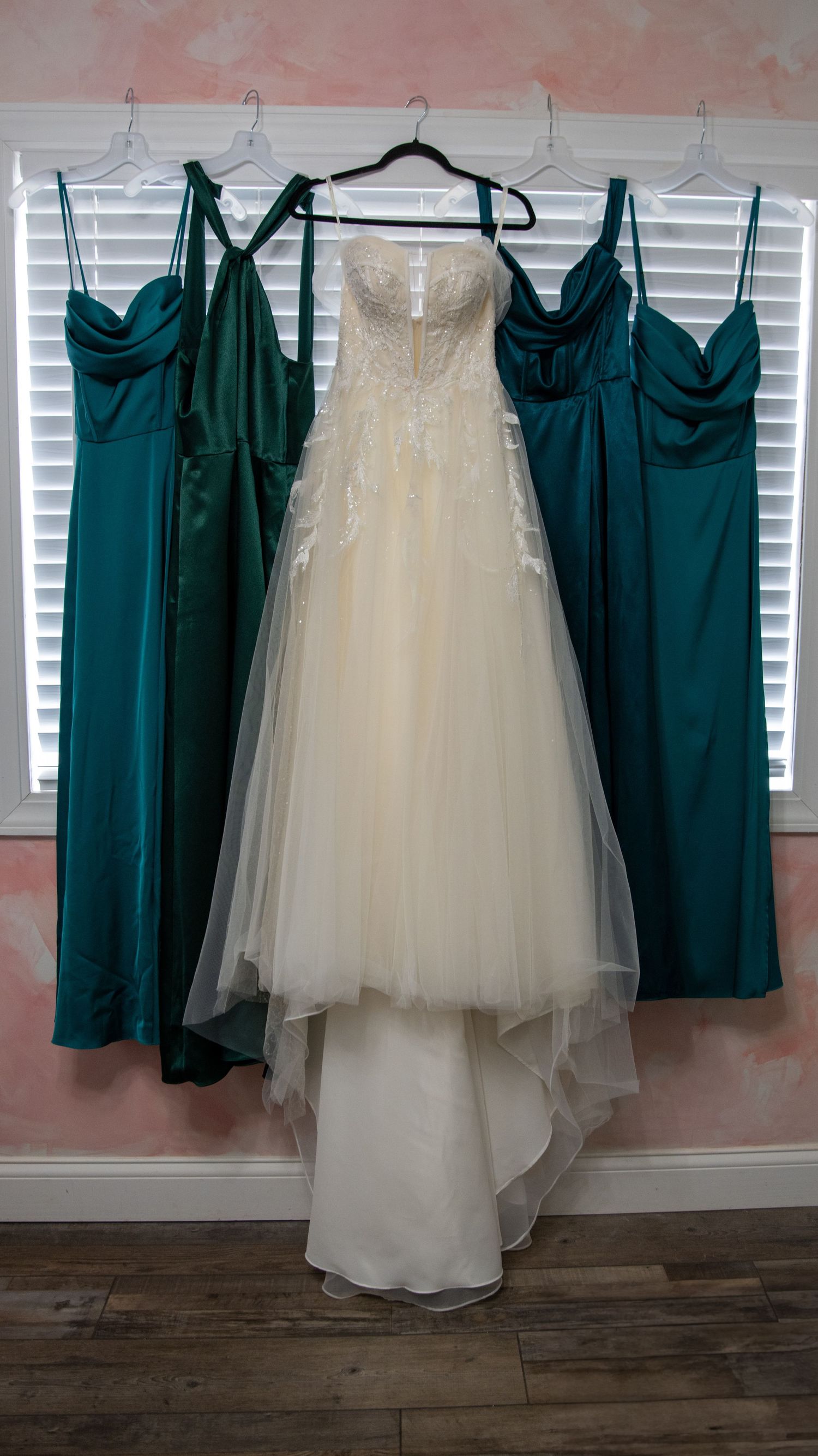 Wedding dress and emerald green bridesmaid dresses hanging on display.