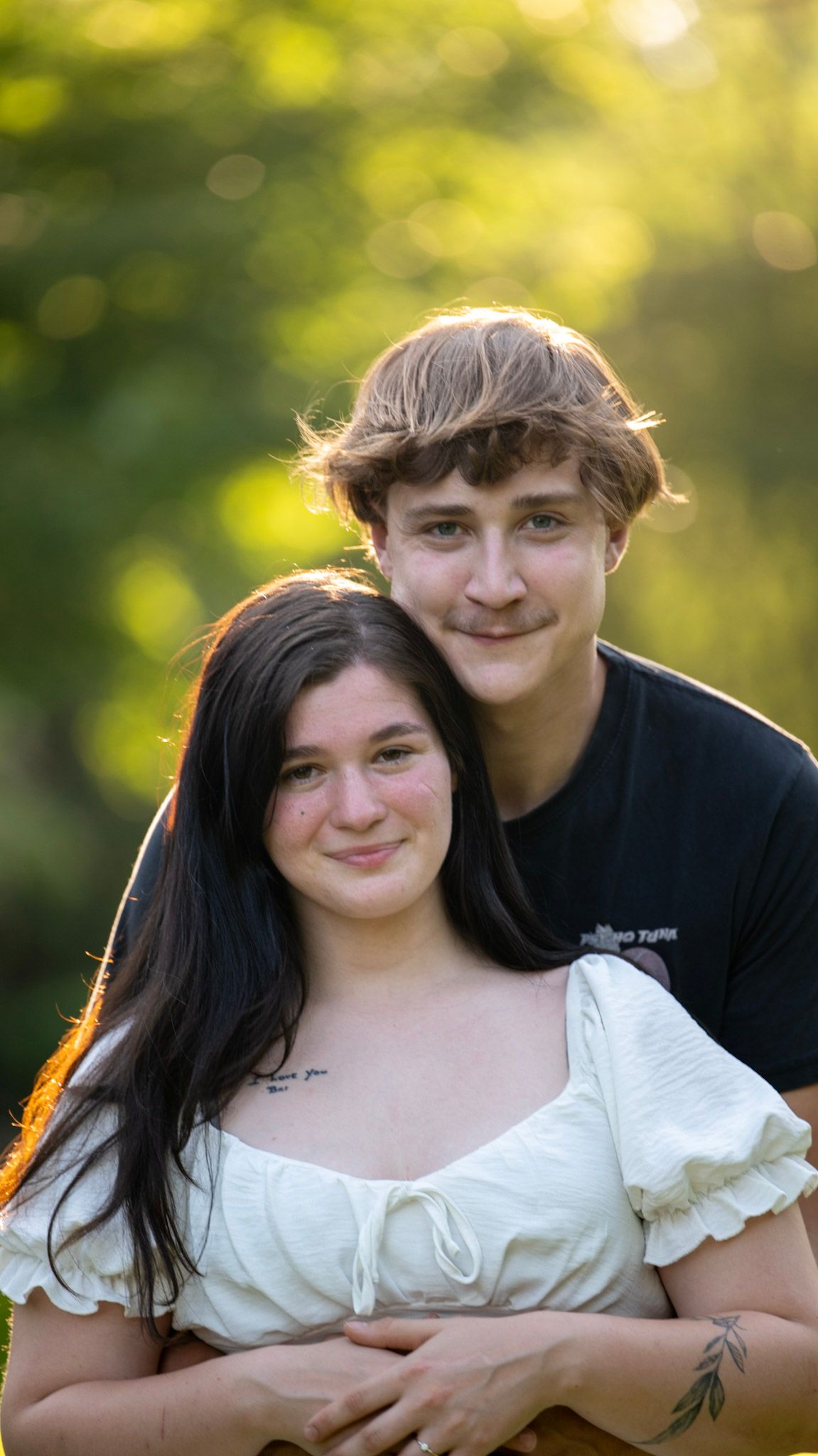 A couple in contrasting black and white outfits pose together in warm sunlight.