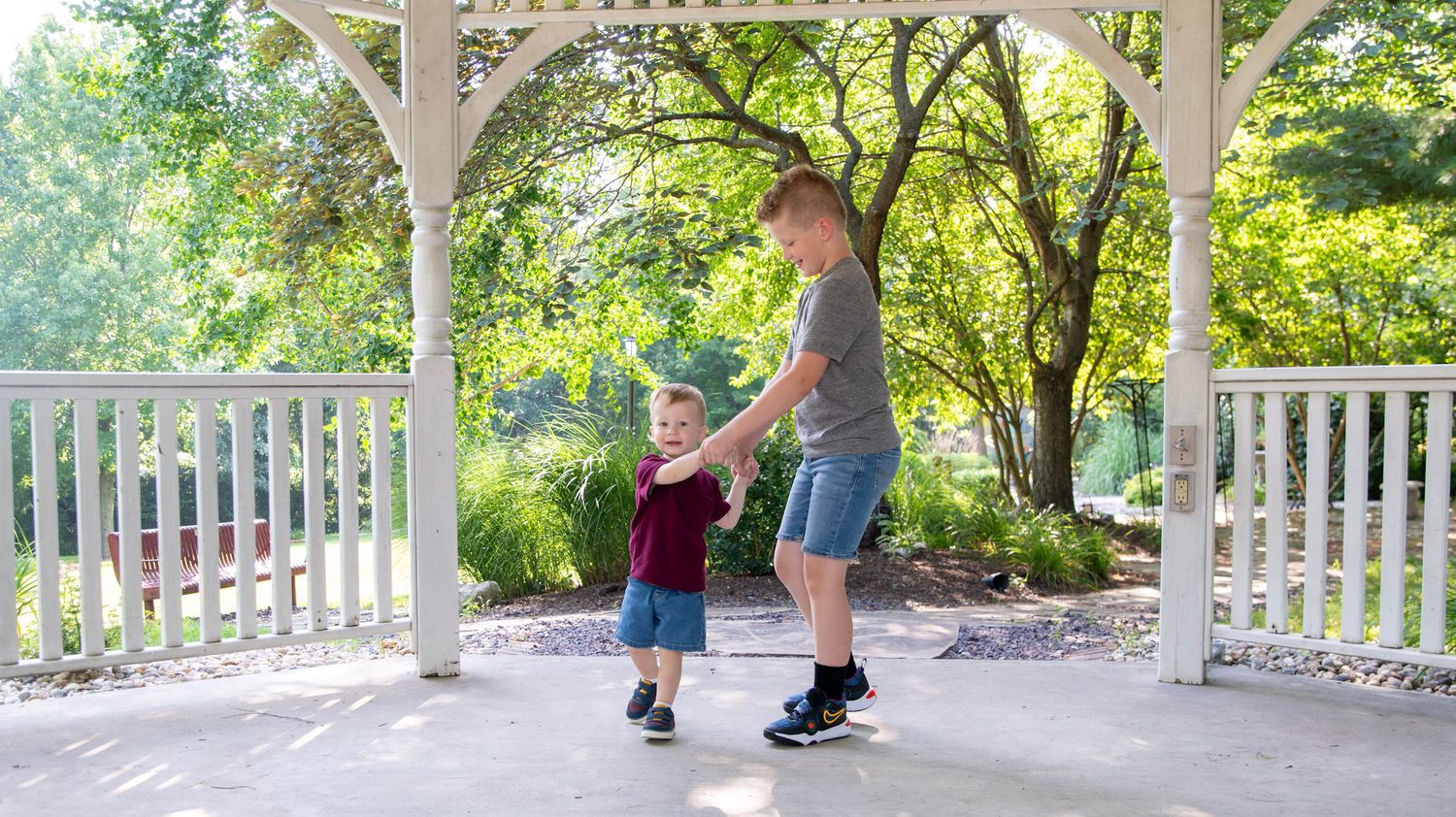 A panoramic view of a white gazebo walkway with lush green trees in the background.