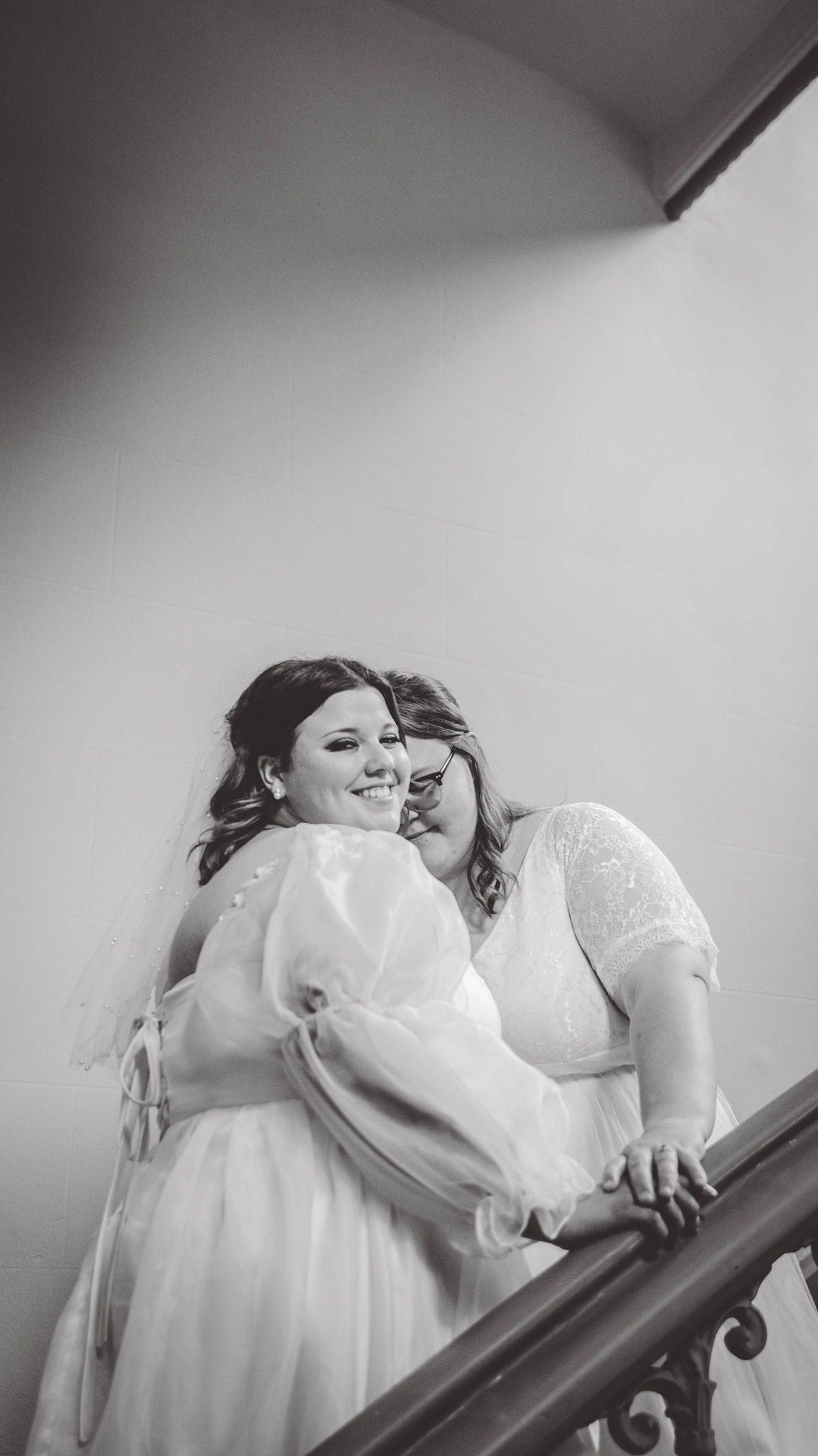 Black and white image of two people in white dresses embracing on a staircase.