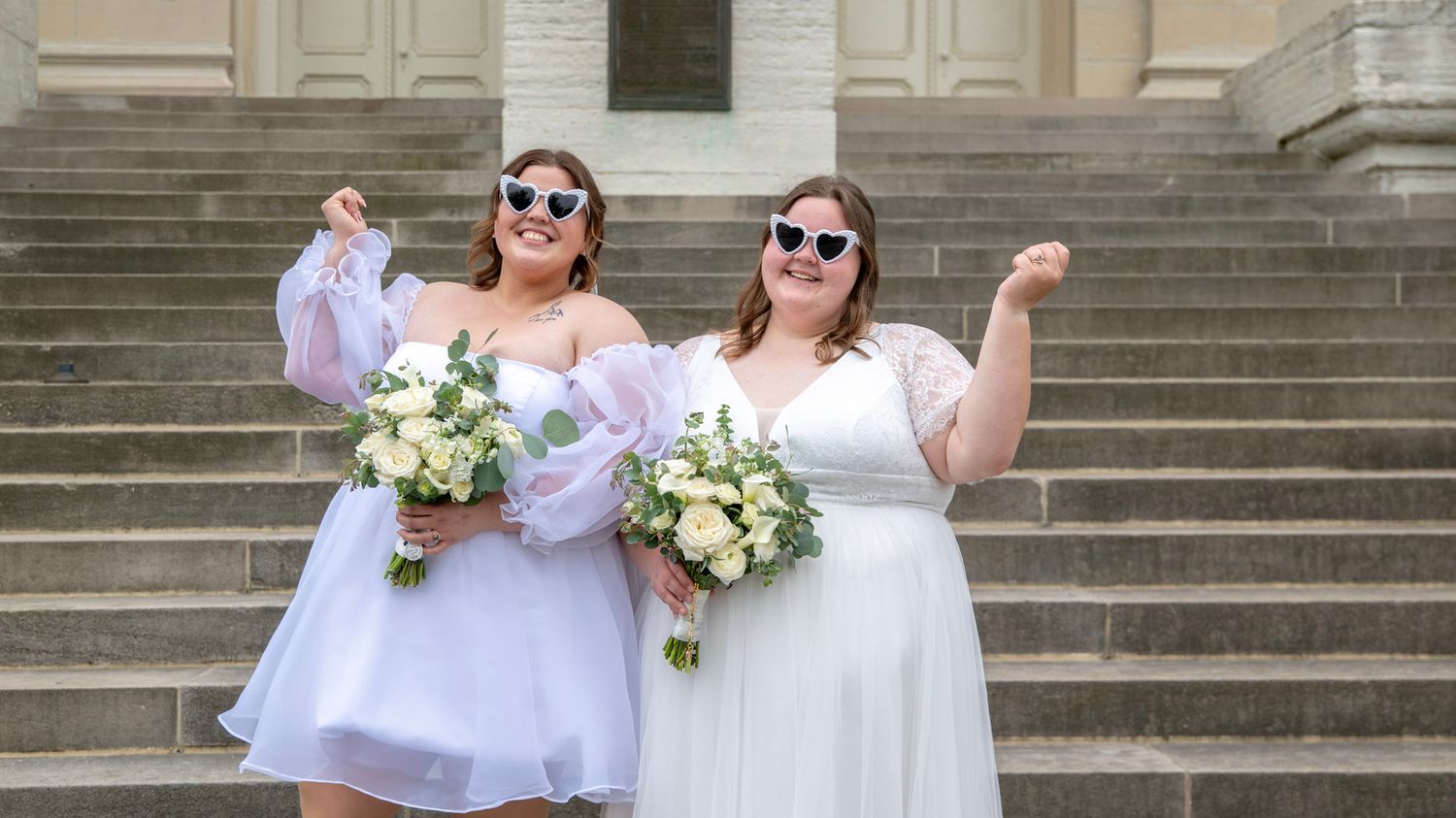 A group poses in white dresses and sunglasses on grand stone steps of a historic building.