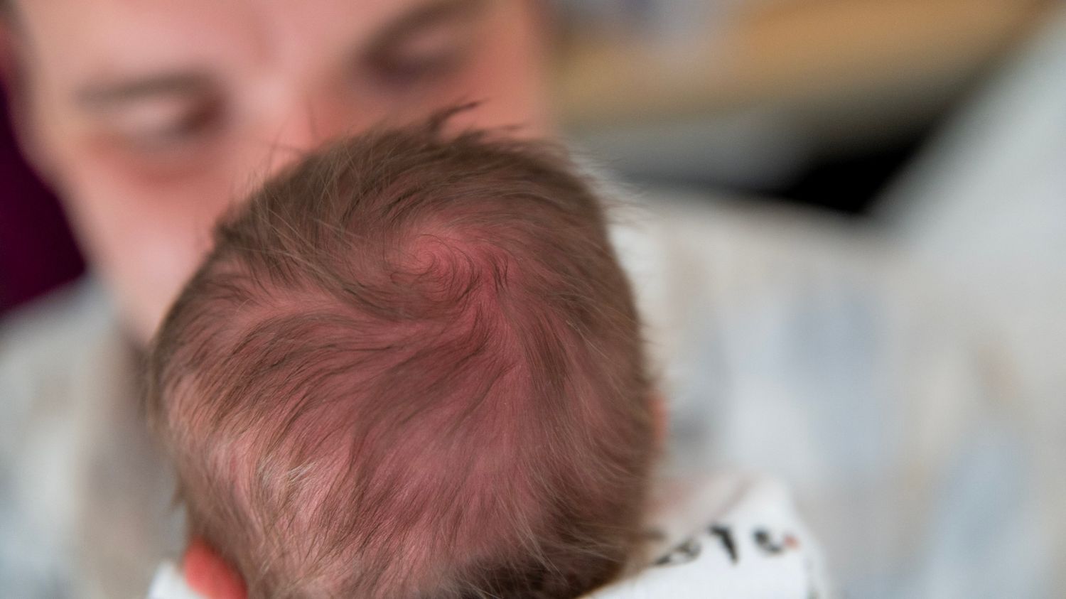 Close-up view of a newborn baby with pink skin being cradled gently.
