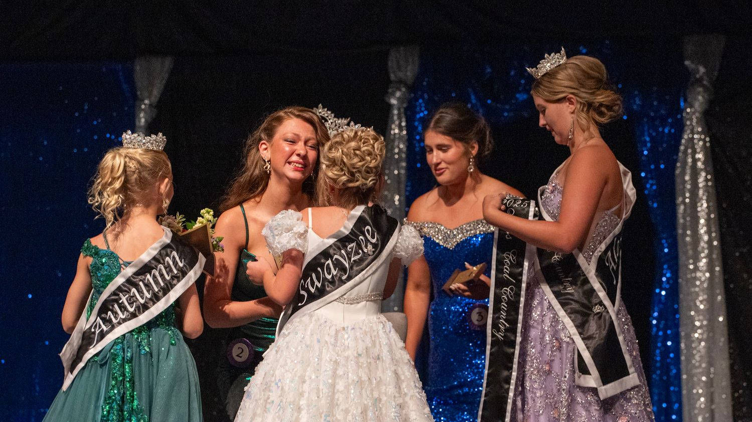 Contestants in formal attire gather on stage during a pageant ceremony.