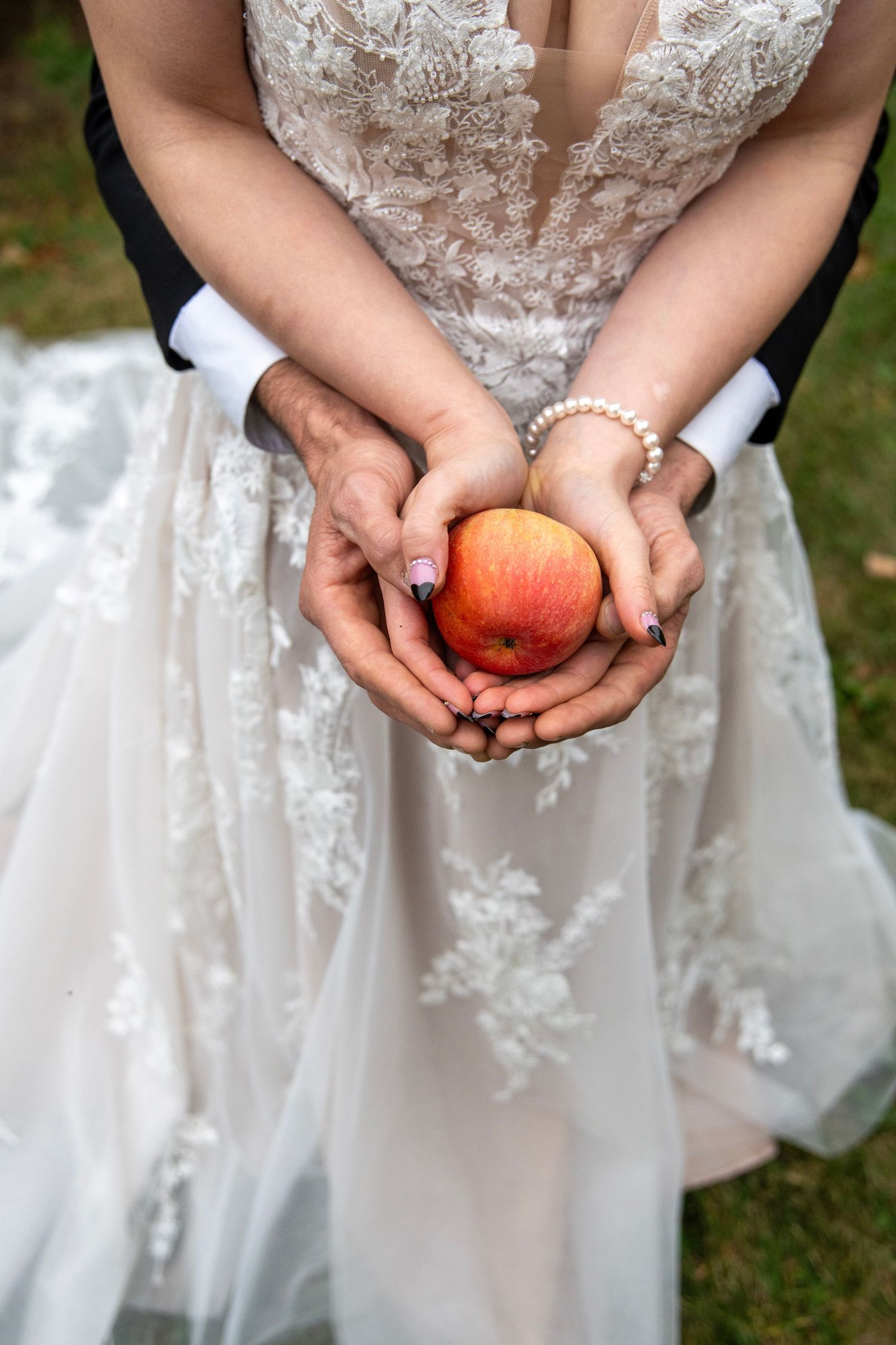 Wedding dress detail with hands holding red apple against lace bodice.