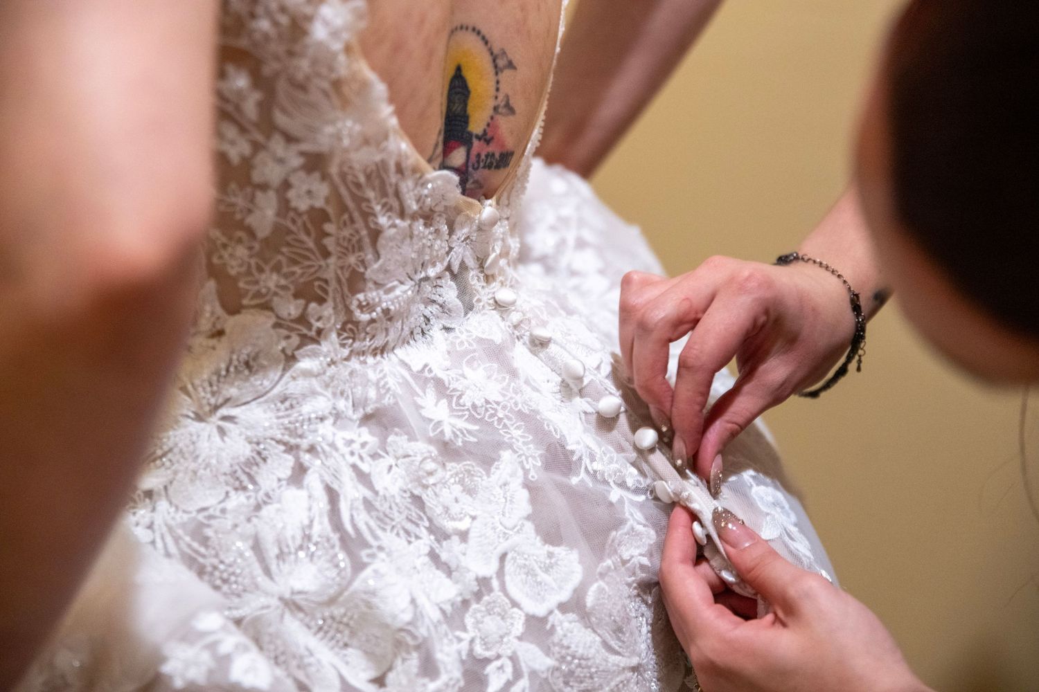 Detail shots of buttons and lace being fastened on the back of a wedding dress.