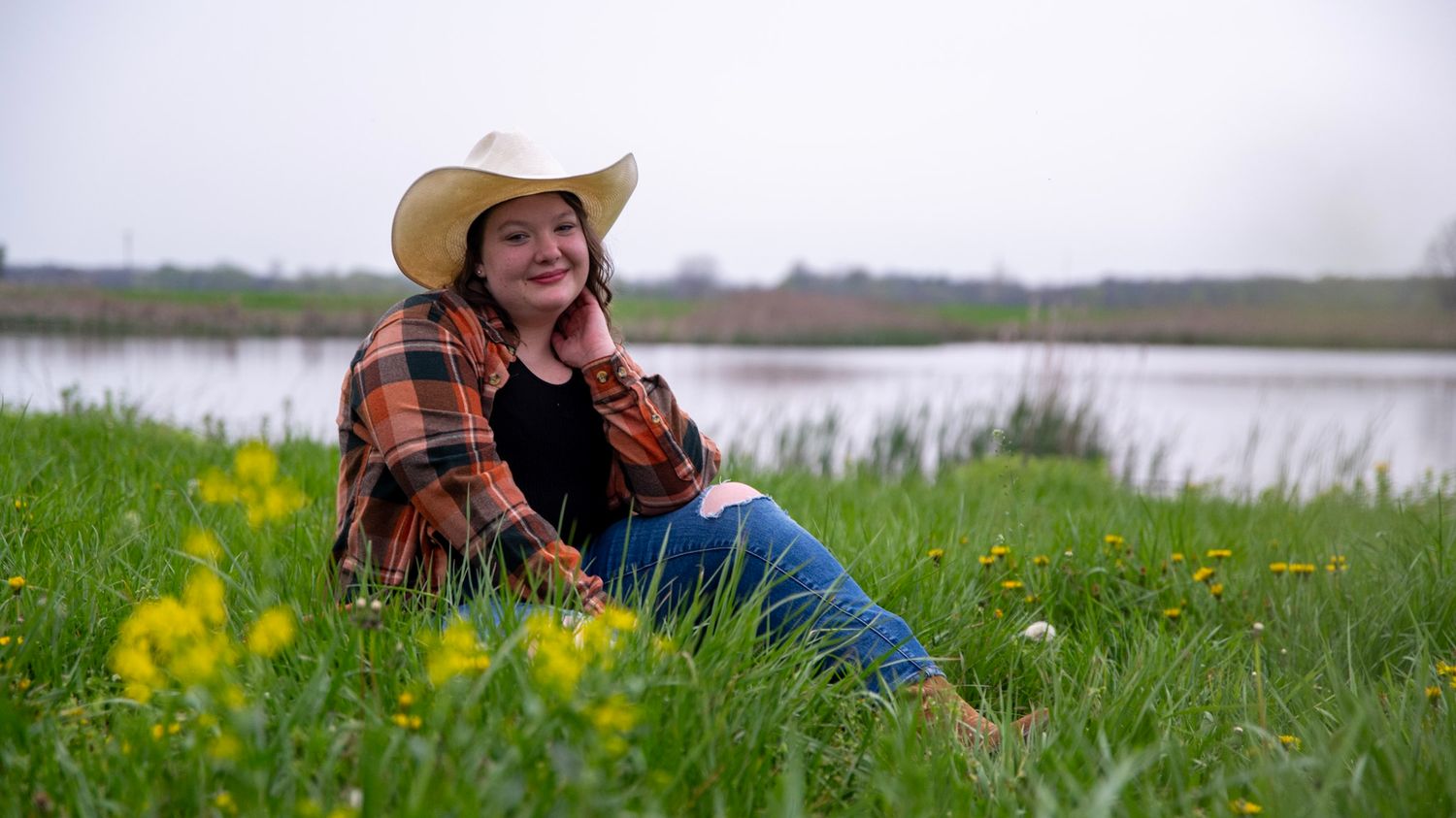 Person in western wear poses in field with yellow wildflowers.