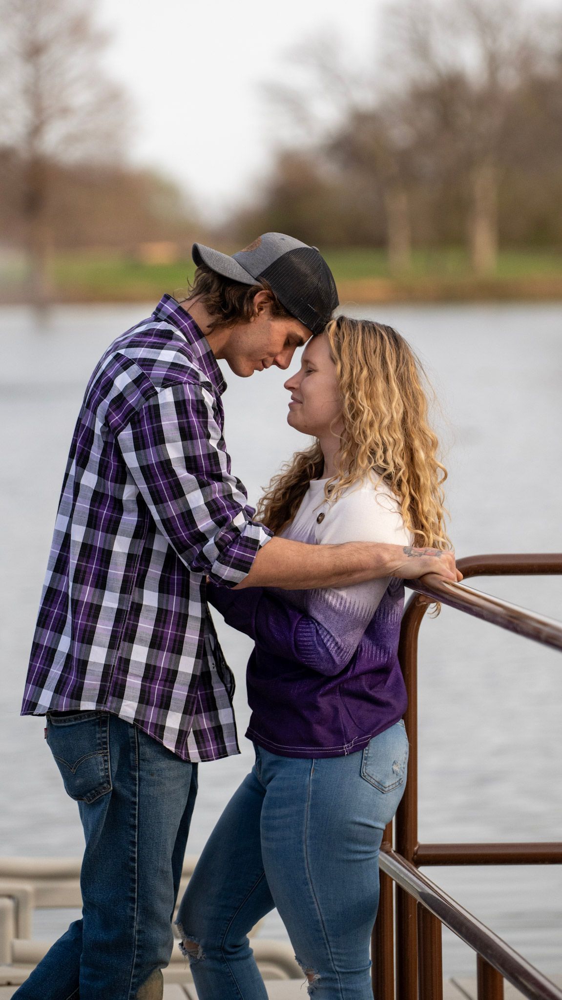 Couple in casual attire sharing intimate moments on a lakeside dock.