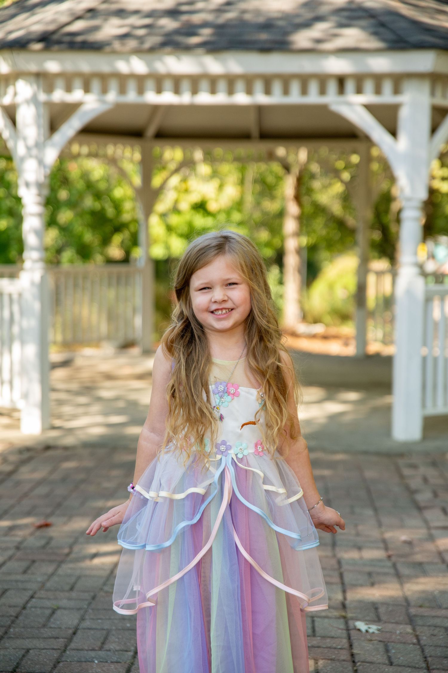 Young girl in a pastel fairy dress twirls and poses under a white garden gazebo.
