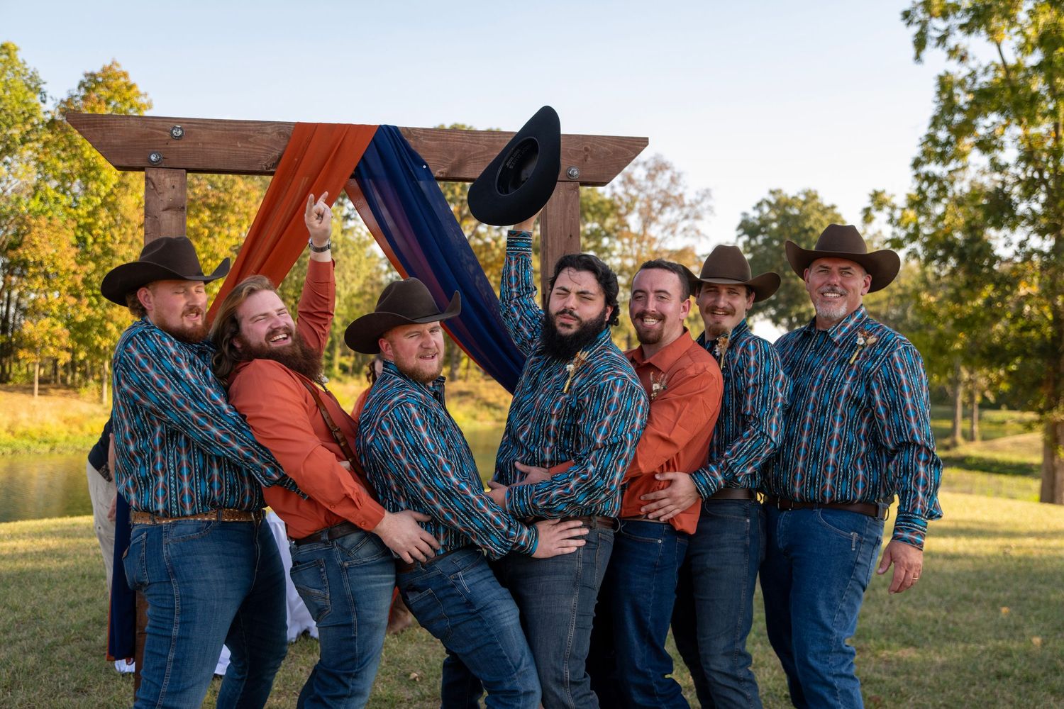 Groomsmen in denim and western attire share a lighthearted moment during outdoor wedding photos.