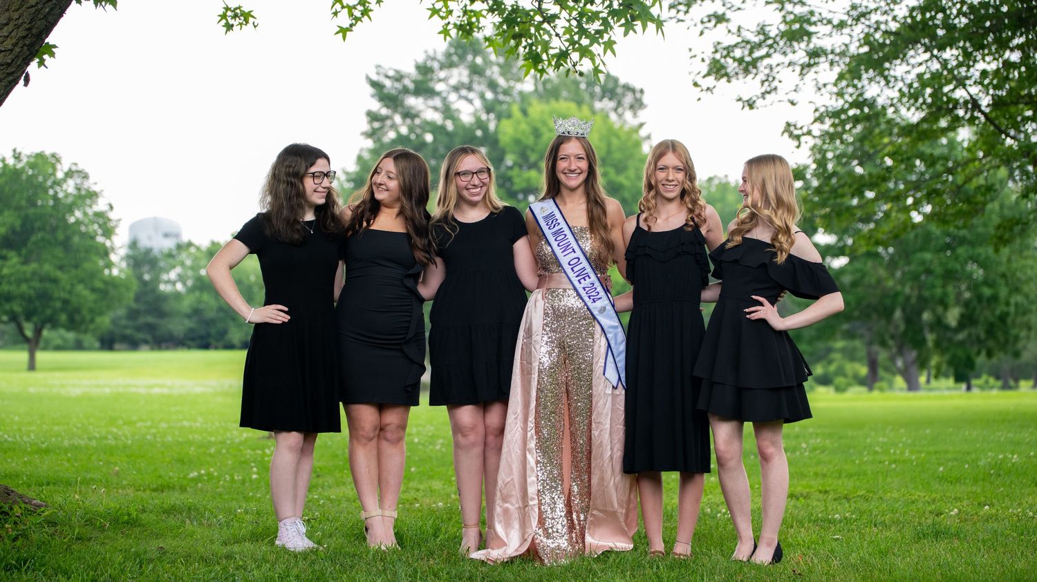 Pageant group photo showing contestants in formal attire against a natural outdoor backdrop.