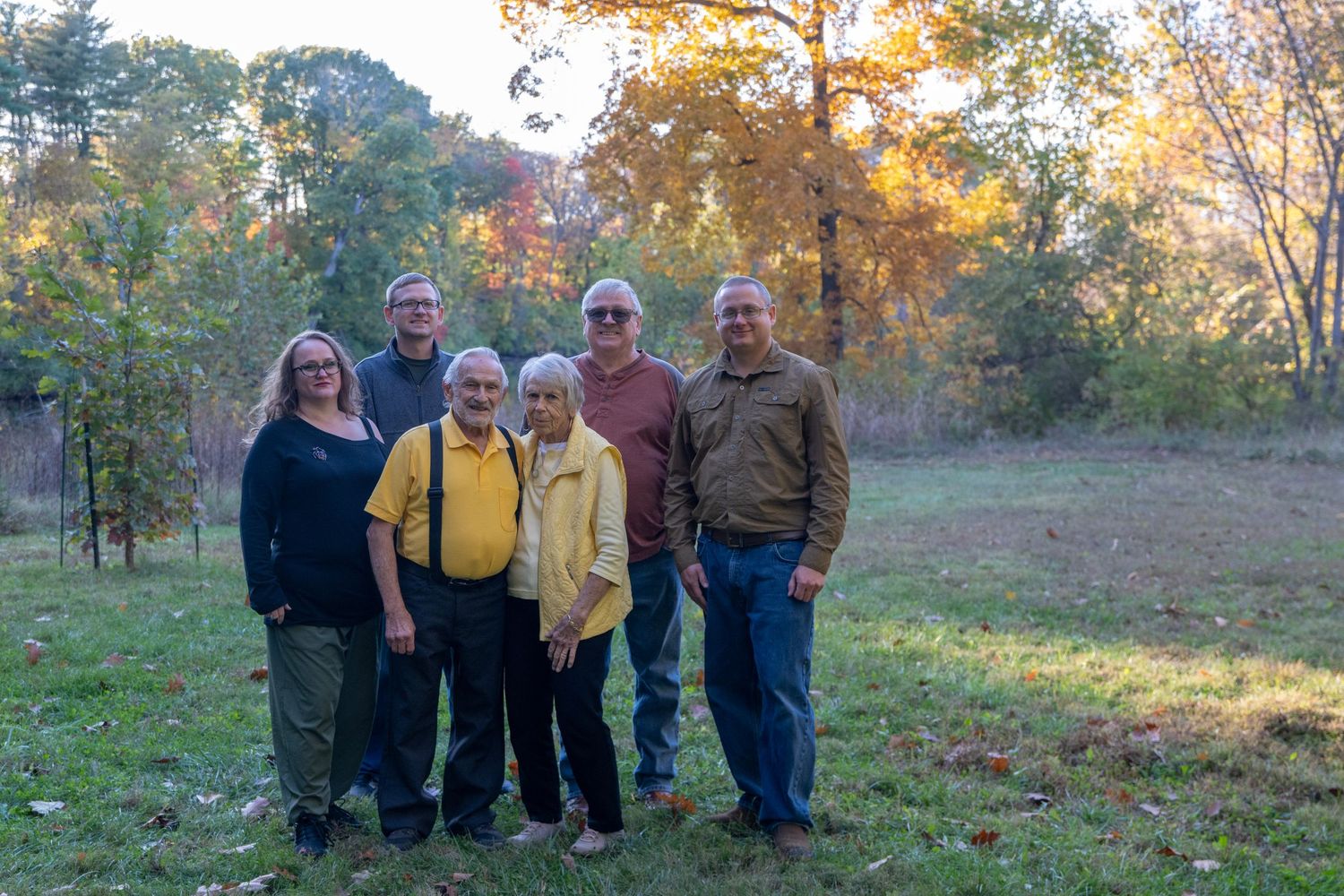 Extended family gathering poses for photo in fall setting with colorful foliage.