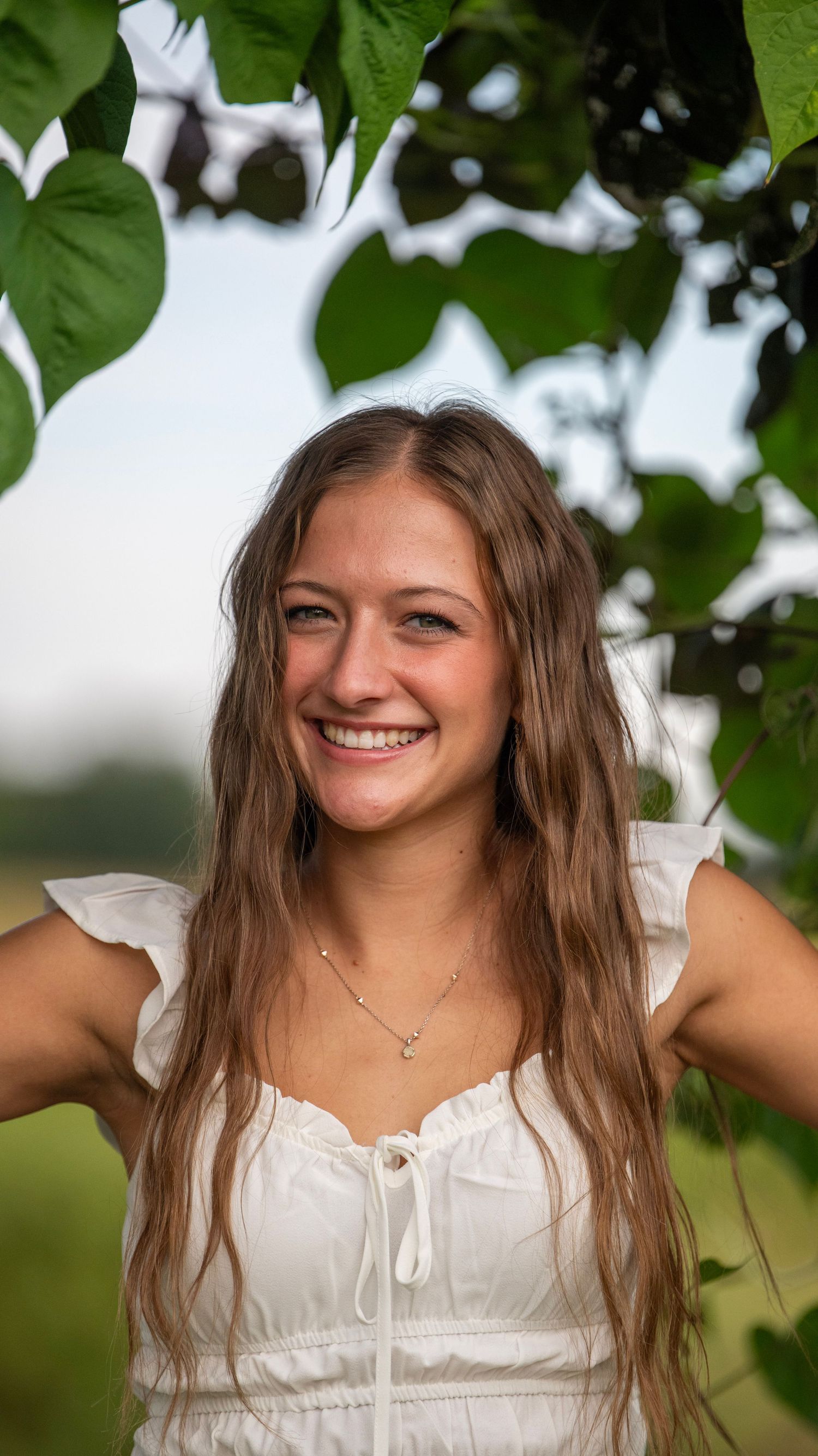 Natural outdoor portrait with someone smiling beneath tree foliage.