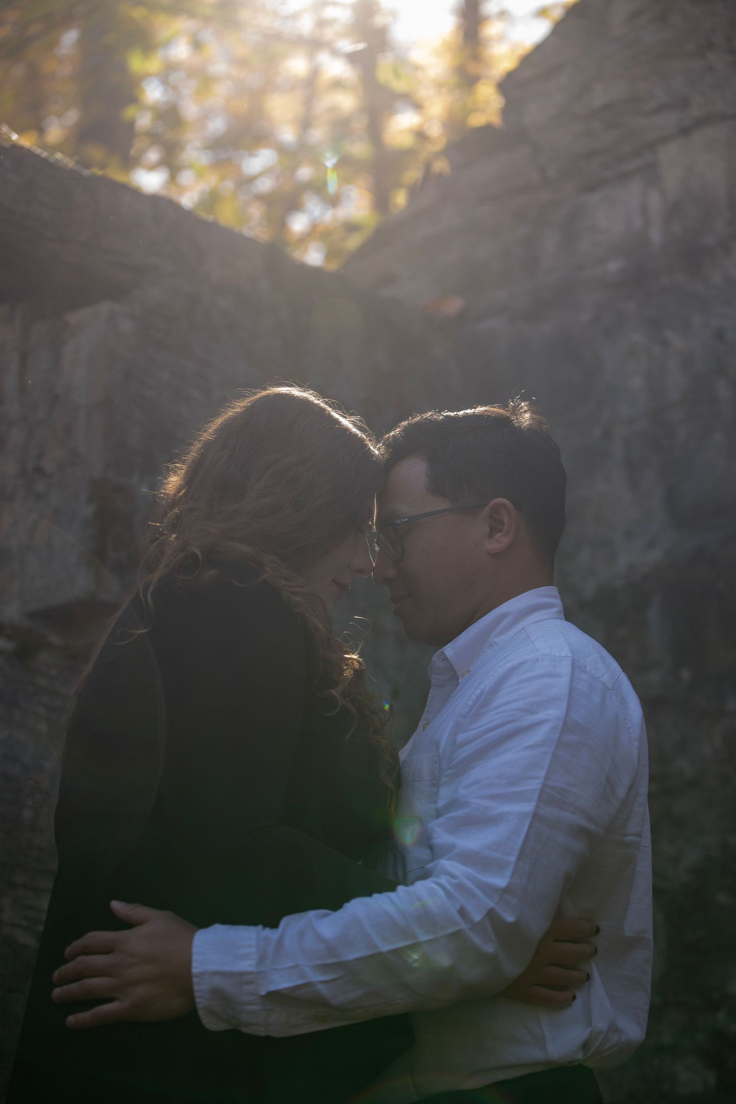 A backlit couple embracing between stone pillars during golden hour.