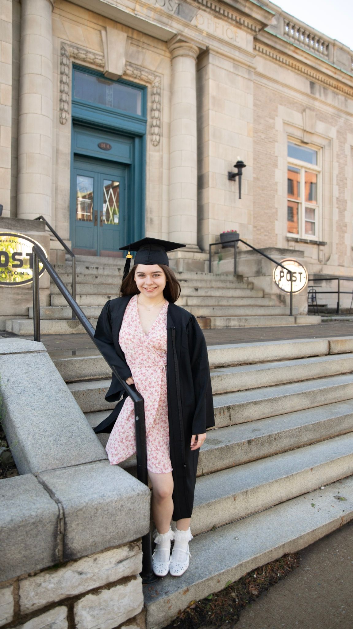 Graduate celebrates on stone steps of academic building wearing cap and gown.
