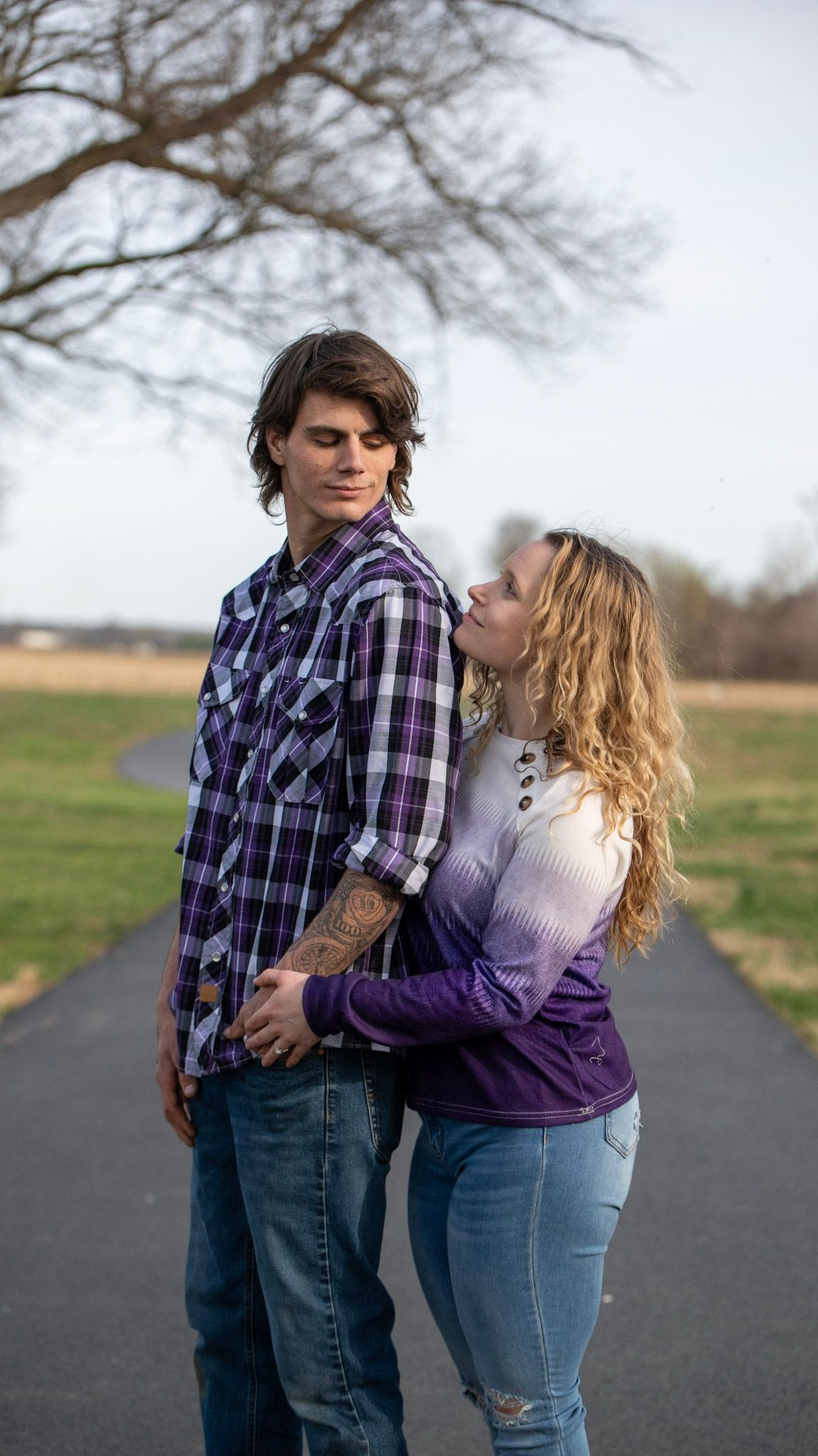 Couple in coordinating purple outfits sharing tender moments on a rural path.
