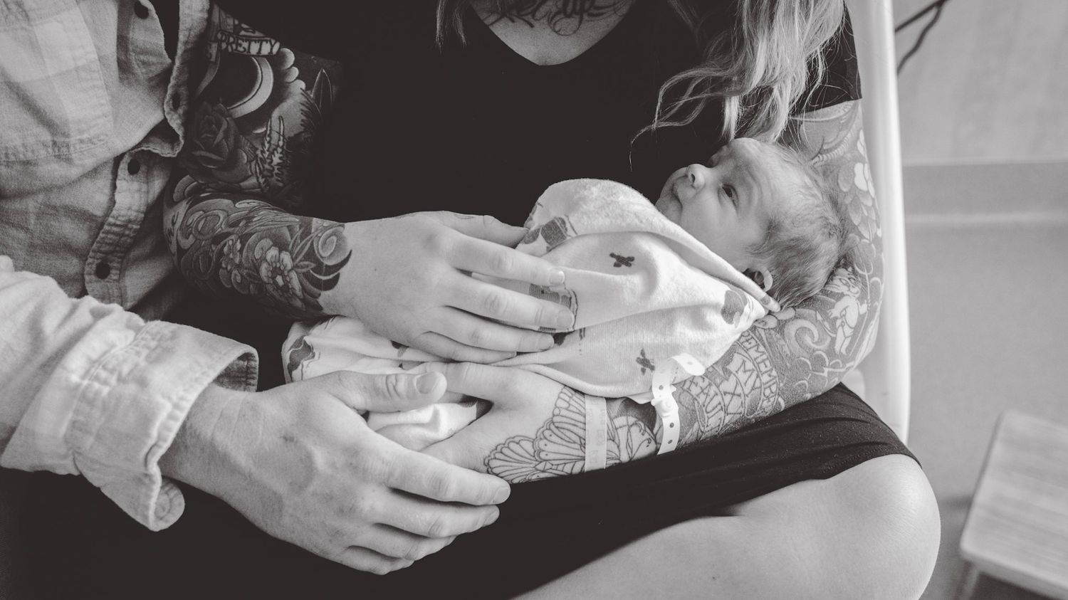 Black and white panorama of parents cradling their newborn baby in a hospital room.