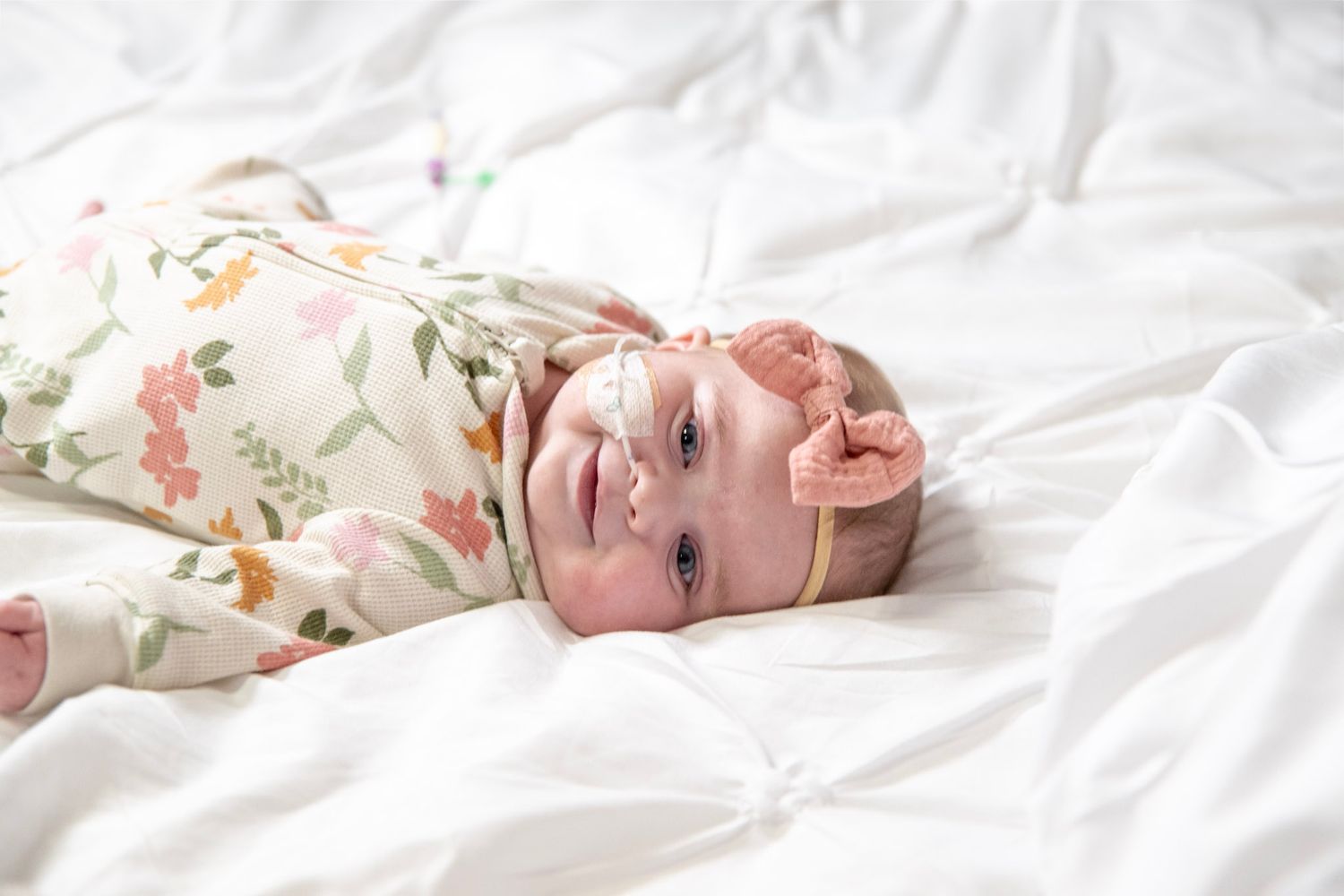 Baby in floral print outfit lying on white fabric during professional photography.
