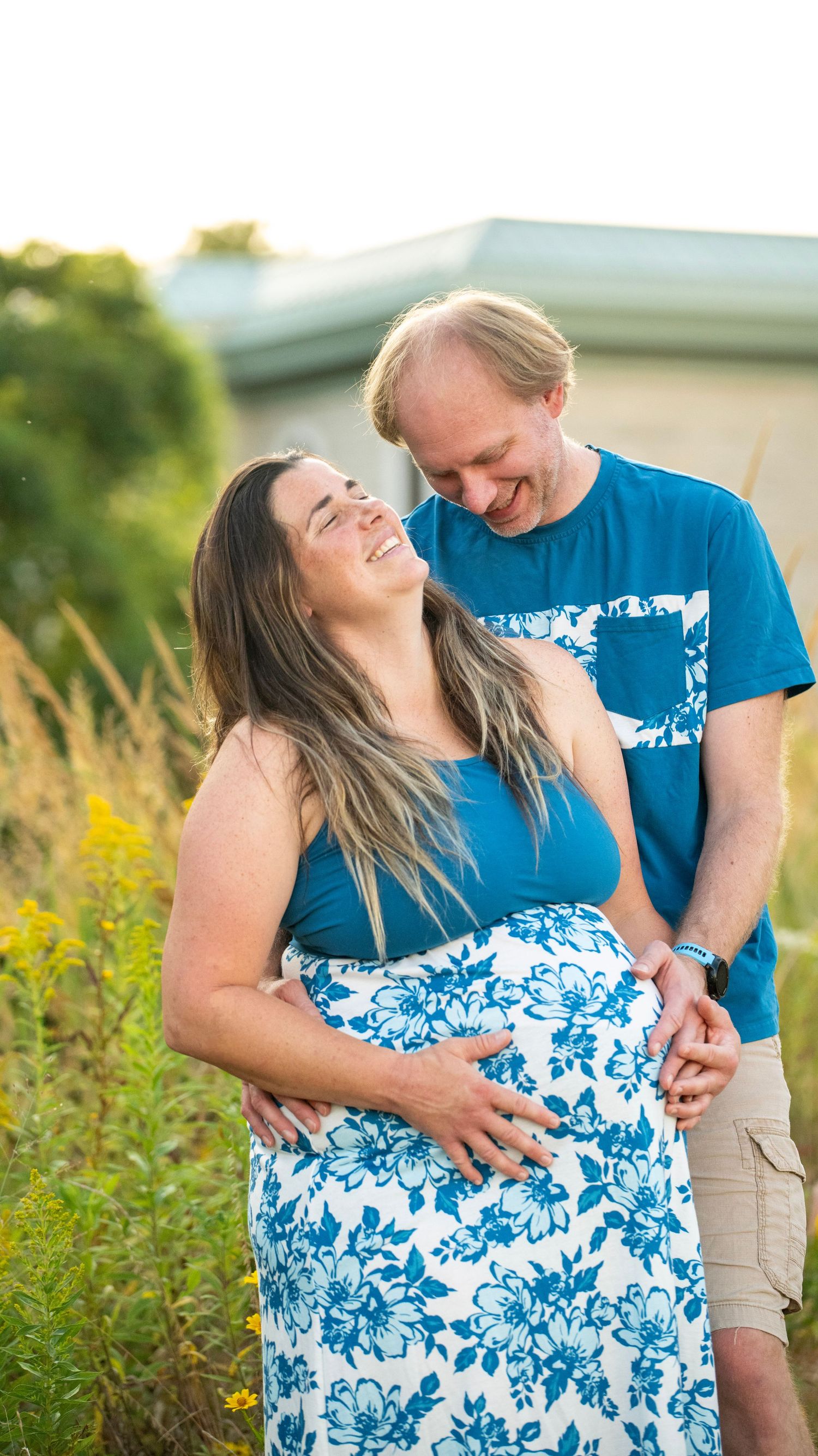 A joyful maternity photoshoot in a field with coordinating blue outfits and floral patterns at sunset.