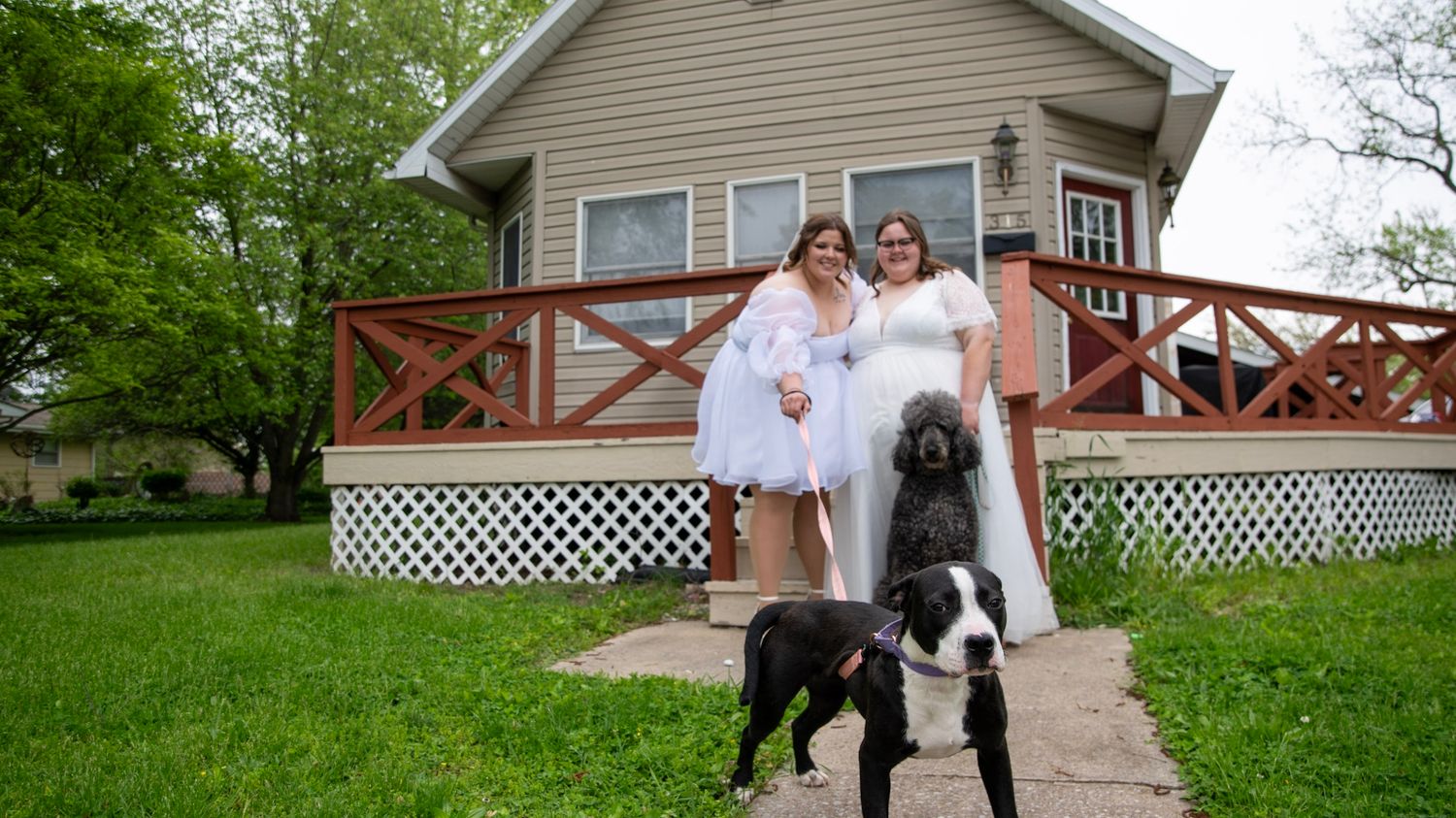 A panoramic view of a beige house exterior with dogs and wedding attire on a spring day.
