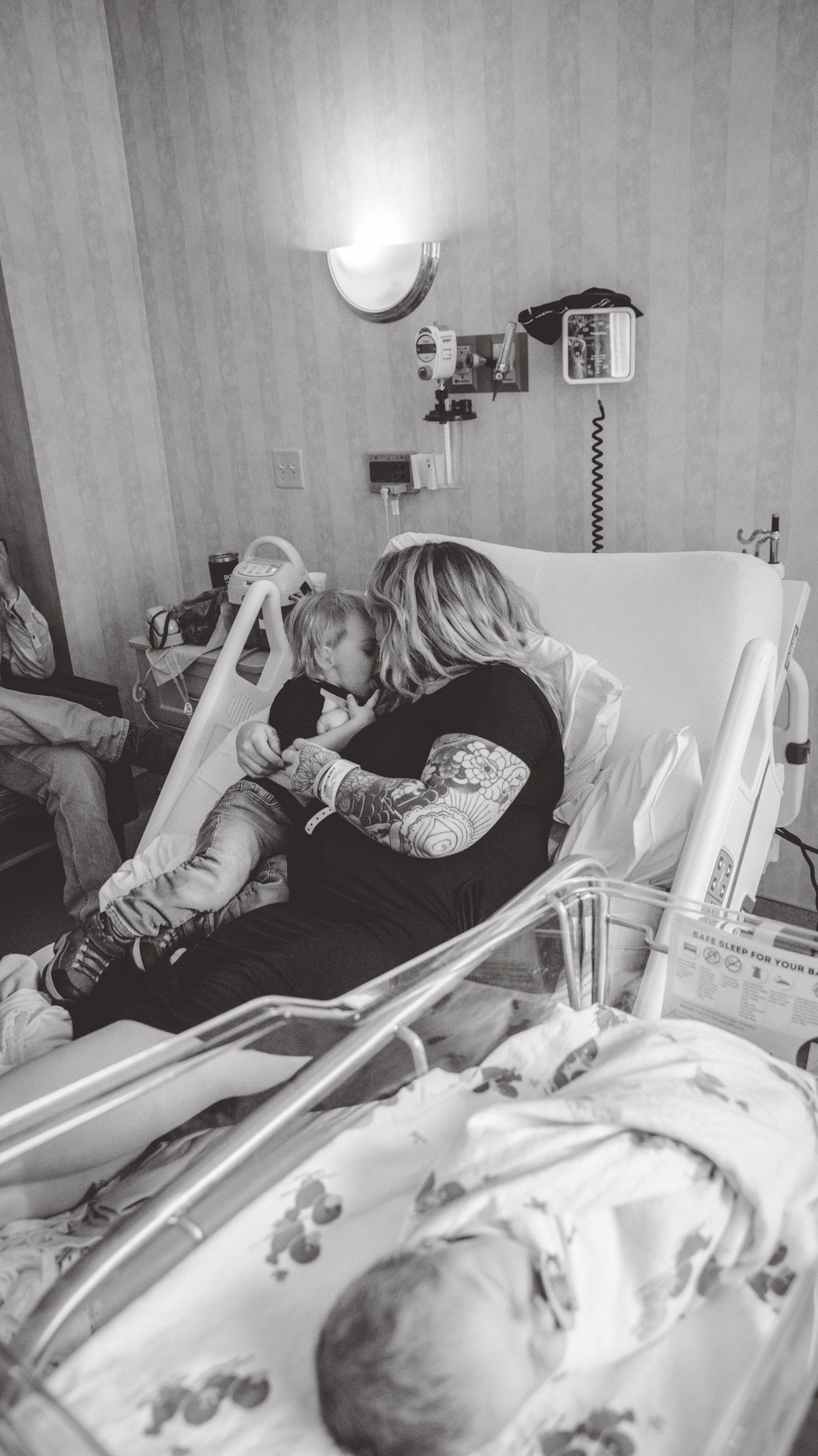 Family resting together on a hospital bed with medical equipment visible.