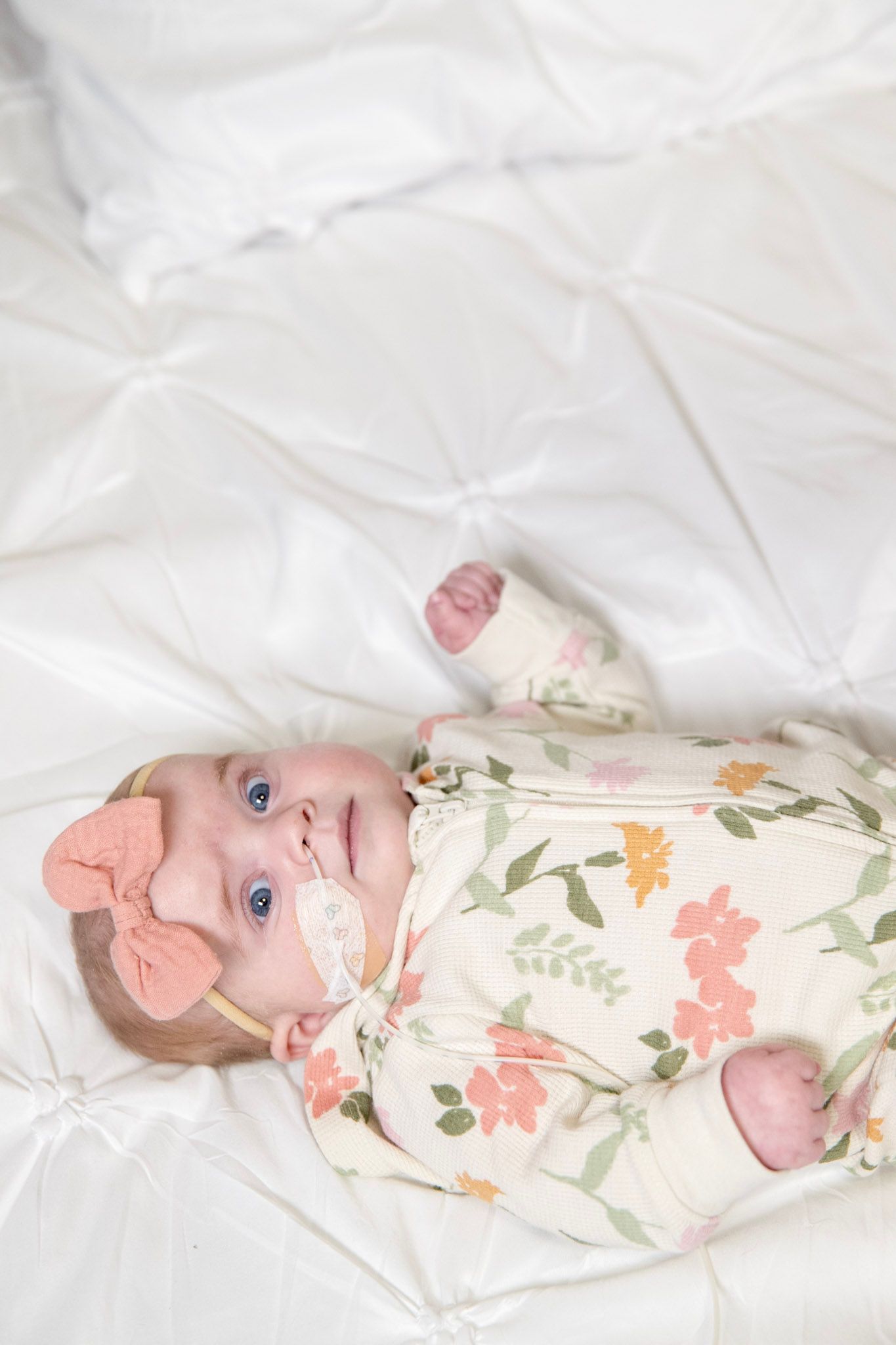 Baby in floral outfit lying on white backdrop during professional photoshoot.