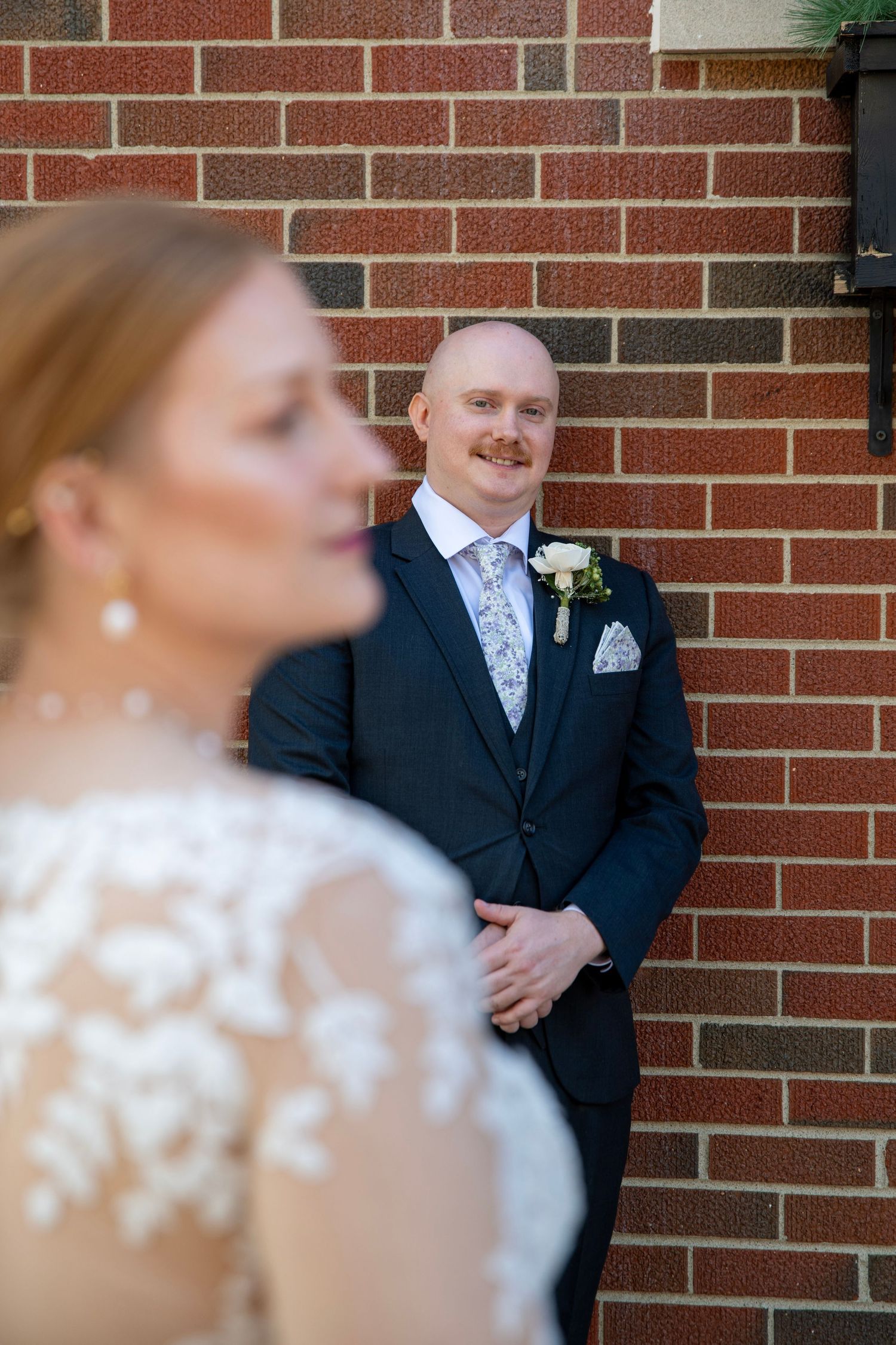 Creative wedding photography with selective focus showing couple against brick wall backdrop.