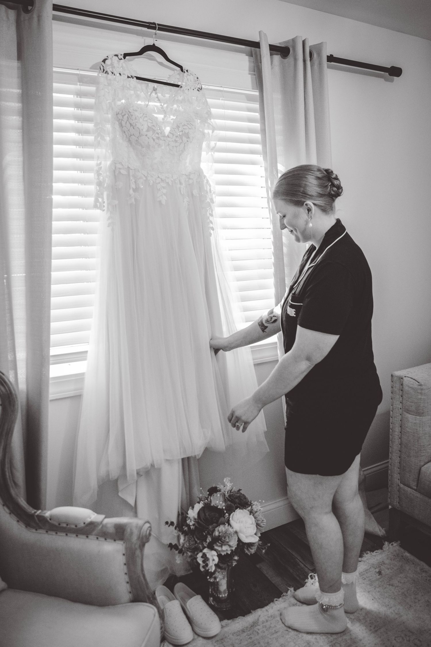 Wedding dress preparation scene with dress hanging by window in bright room.