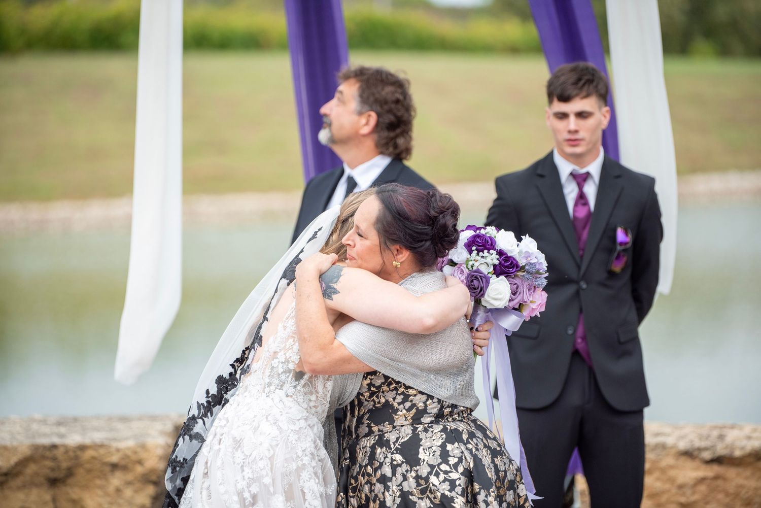 Emotional moment during lakeside wedding ceremony with attendees in formal attire.