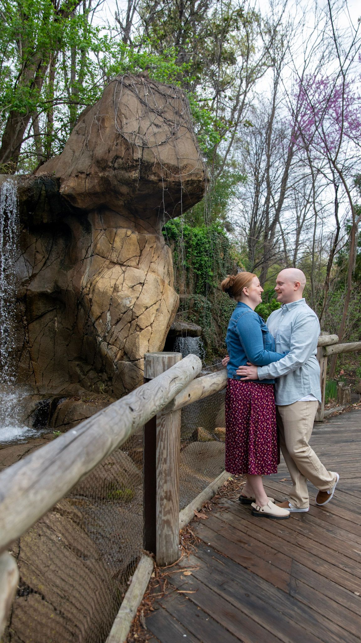 A couple shares intimate moments on a wooden walkway near rocky cliffs and spring foliage.
