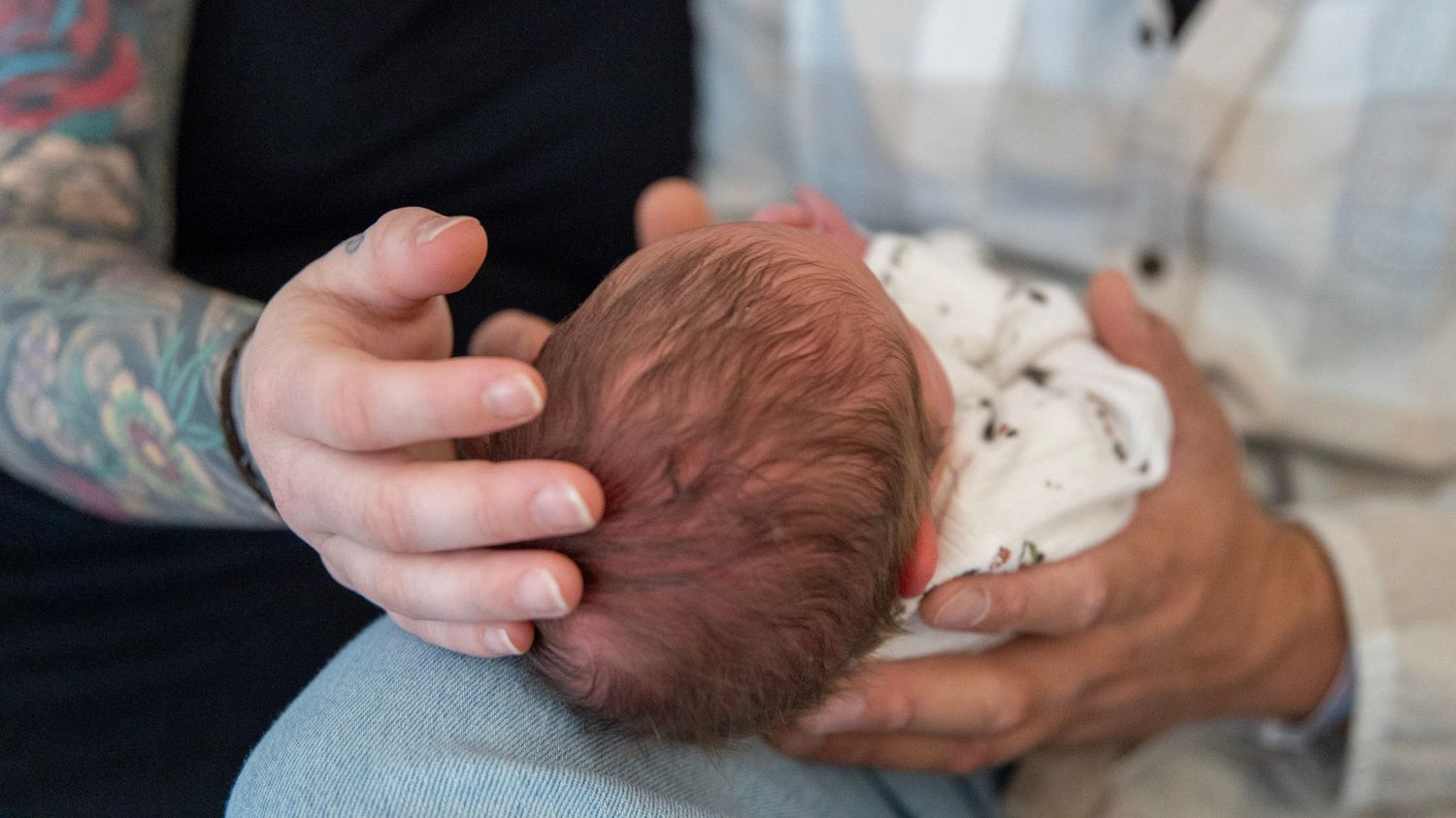 Close-up details of hands gently cradling a newborn baby's head.