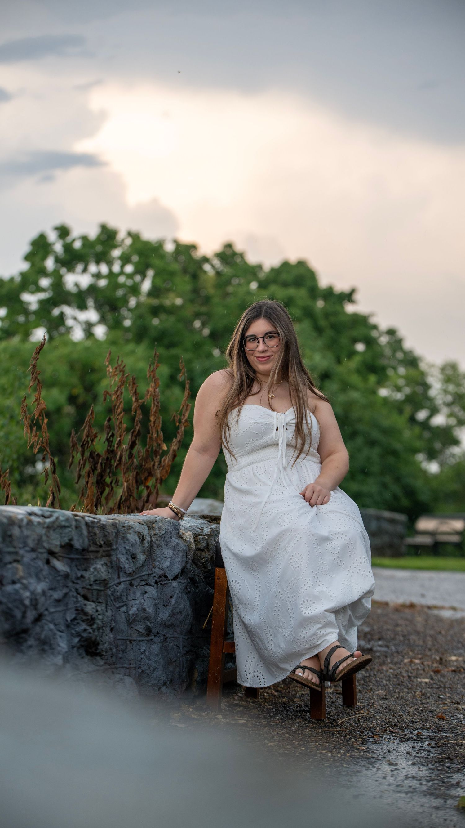 Person in white dress sits on stone wall during golden hour photoshoot.