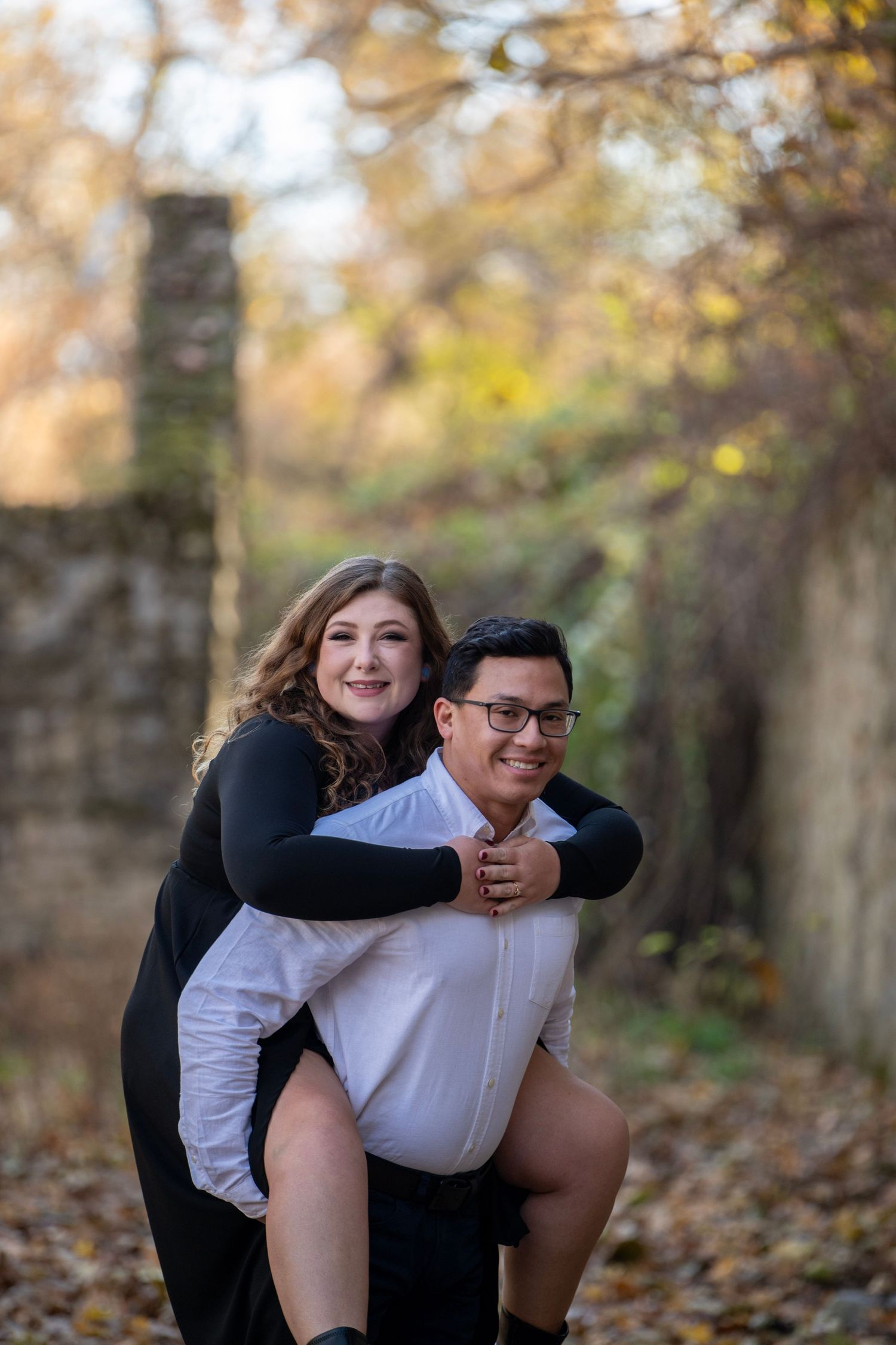 Playful couple shares joyful moment among fallen autumn leaves by stone wall.