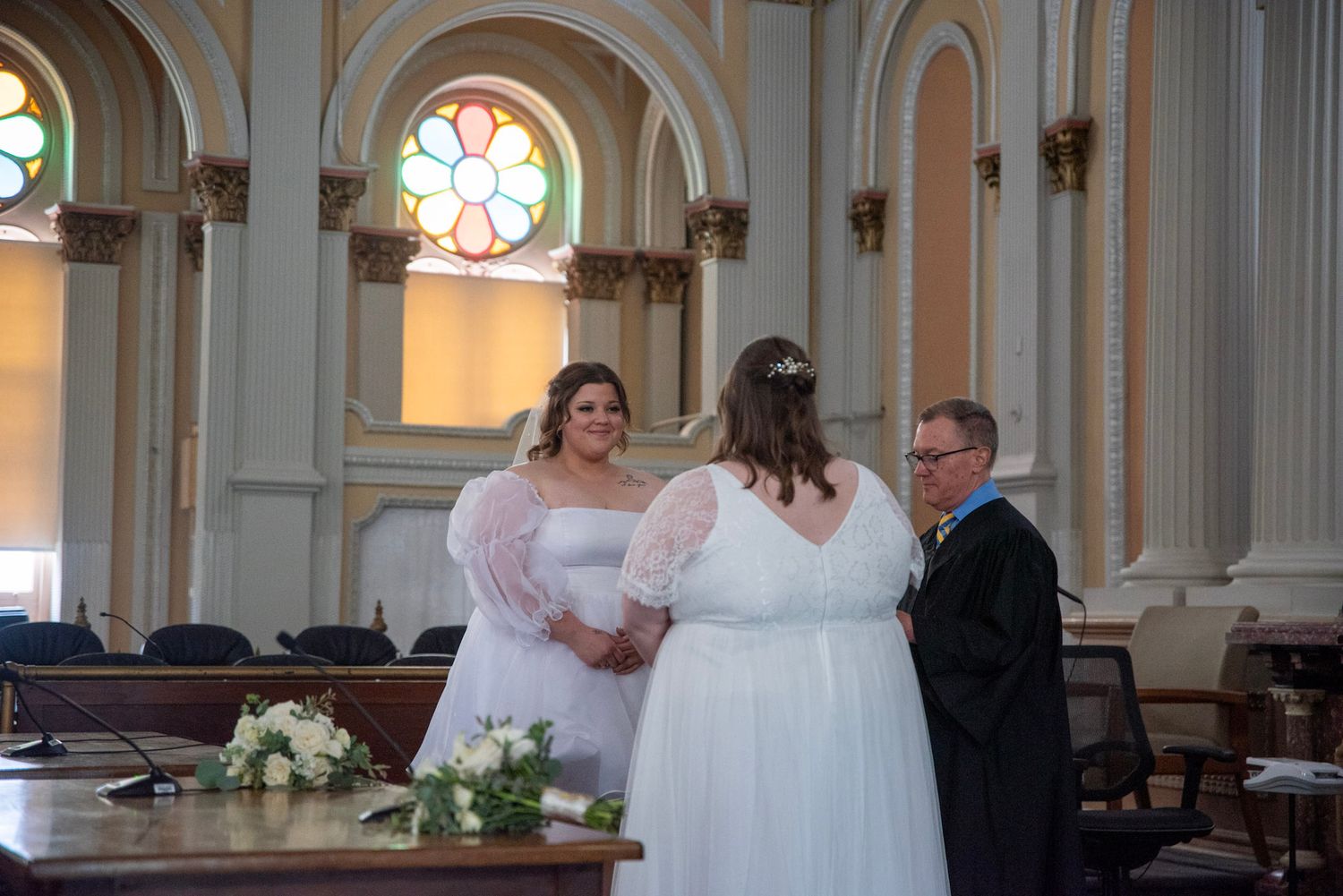 Wedding party gathered at the altar of a grand church with decorative columns and arches.