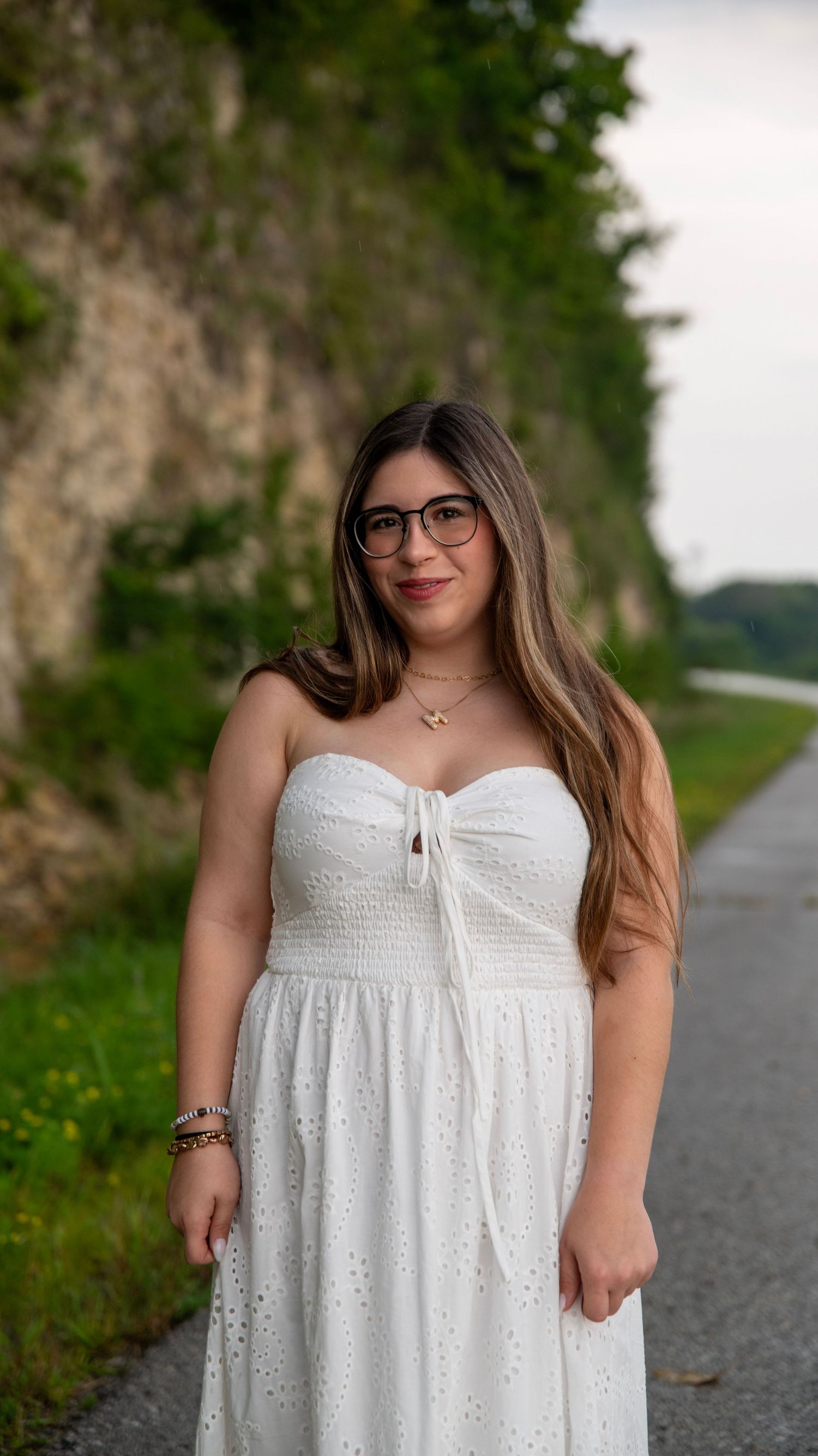 Model in white summer dress poses along stone path during outdoor photoshoot.
