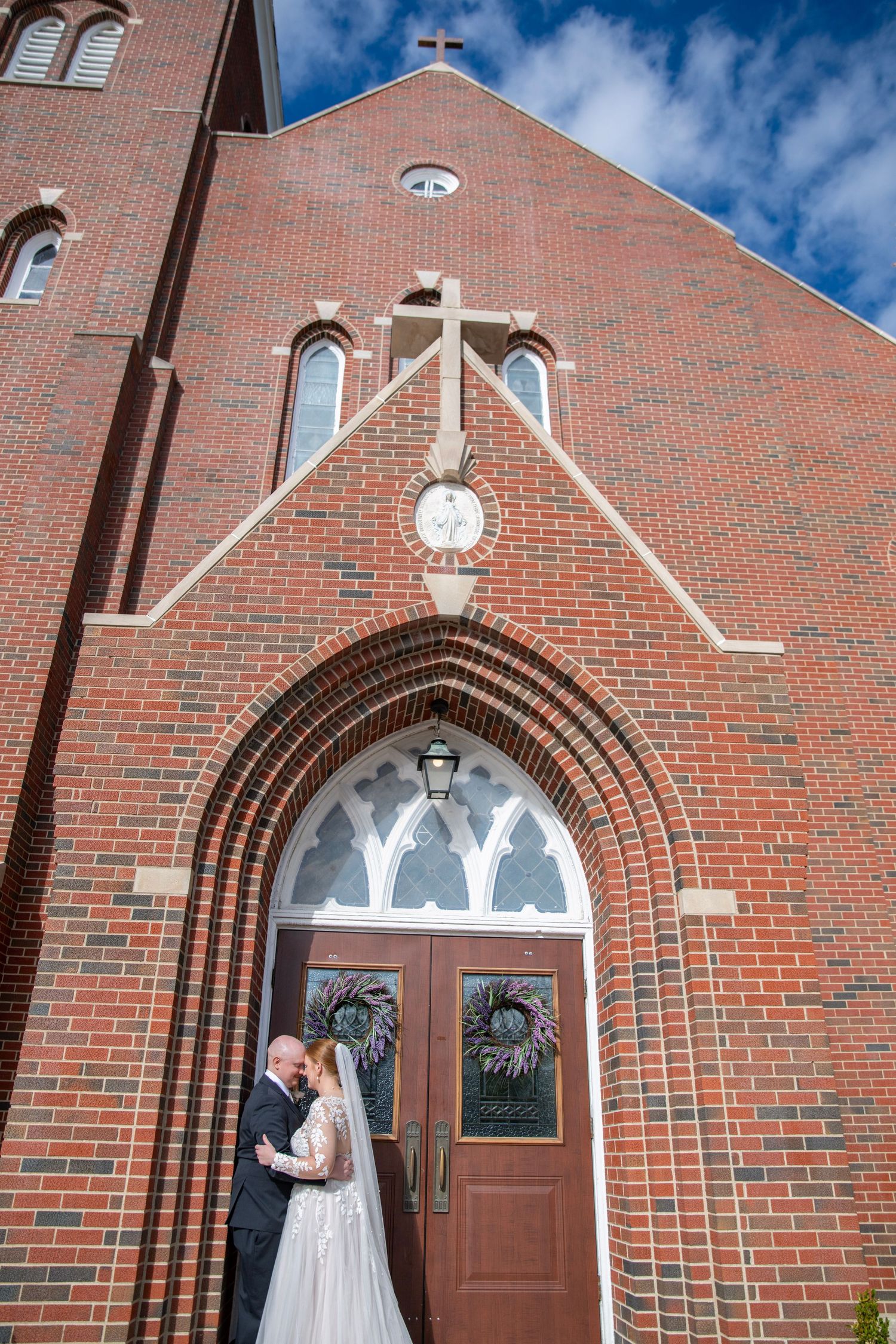 A red brick church exterior with arched doorways and white trim details against a bright blue sky.