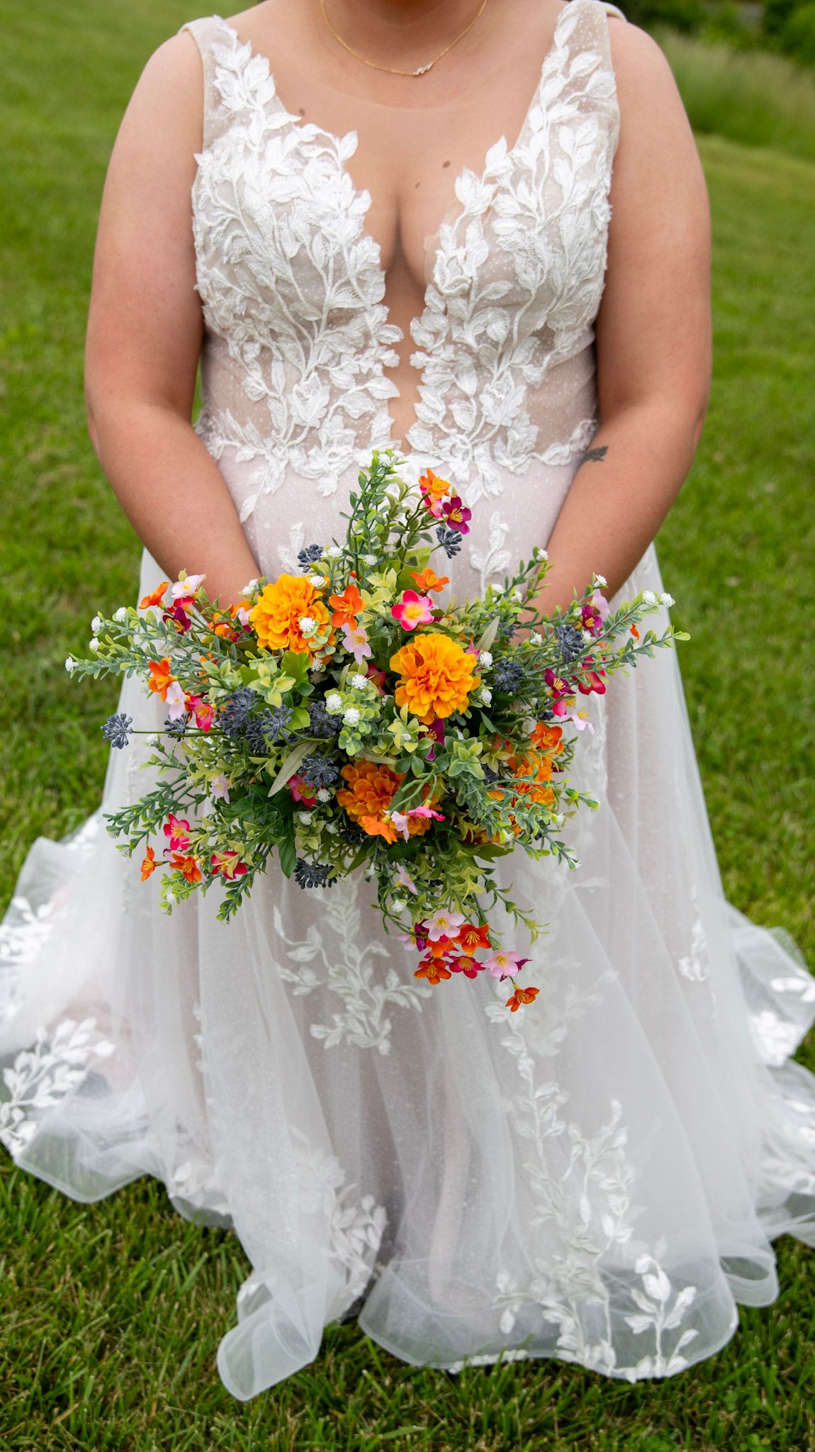Colorful wildflower wedding bouquet held against a white lace wedding dress.